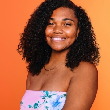 Smiling person with curly hair in a strapless floral top against an orange background