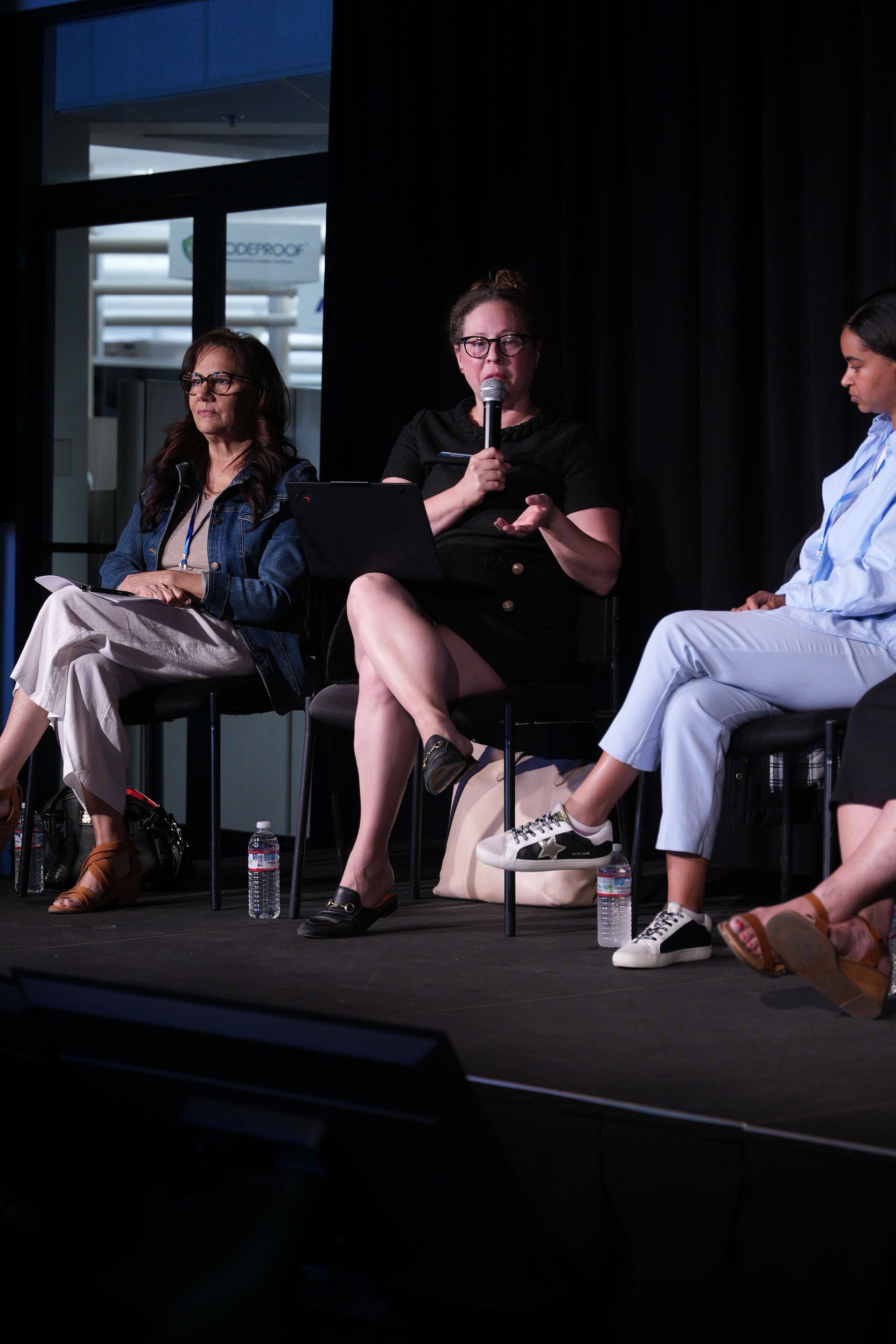Three people seated onstage in a panel discussion, with one speaking into a microphone.