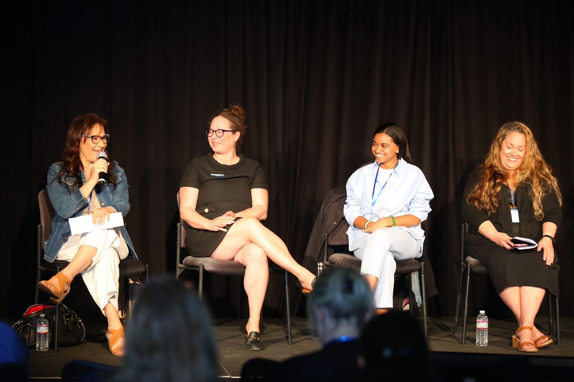 Four speakers seated on a stage in front of black curtains, taking part in a panel discussion.