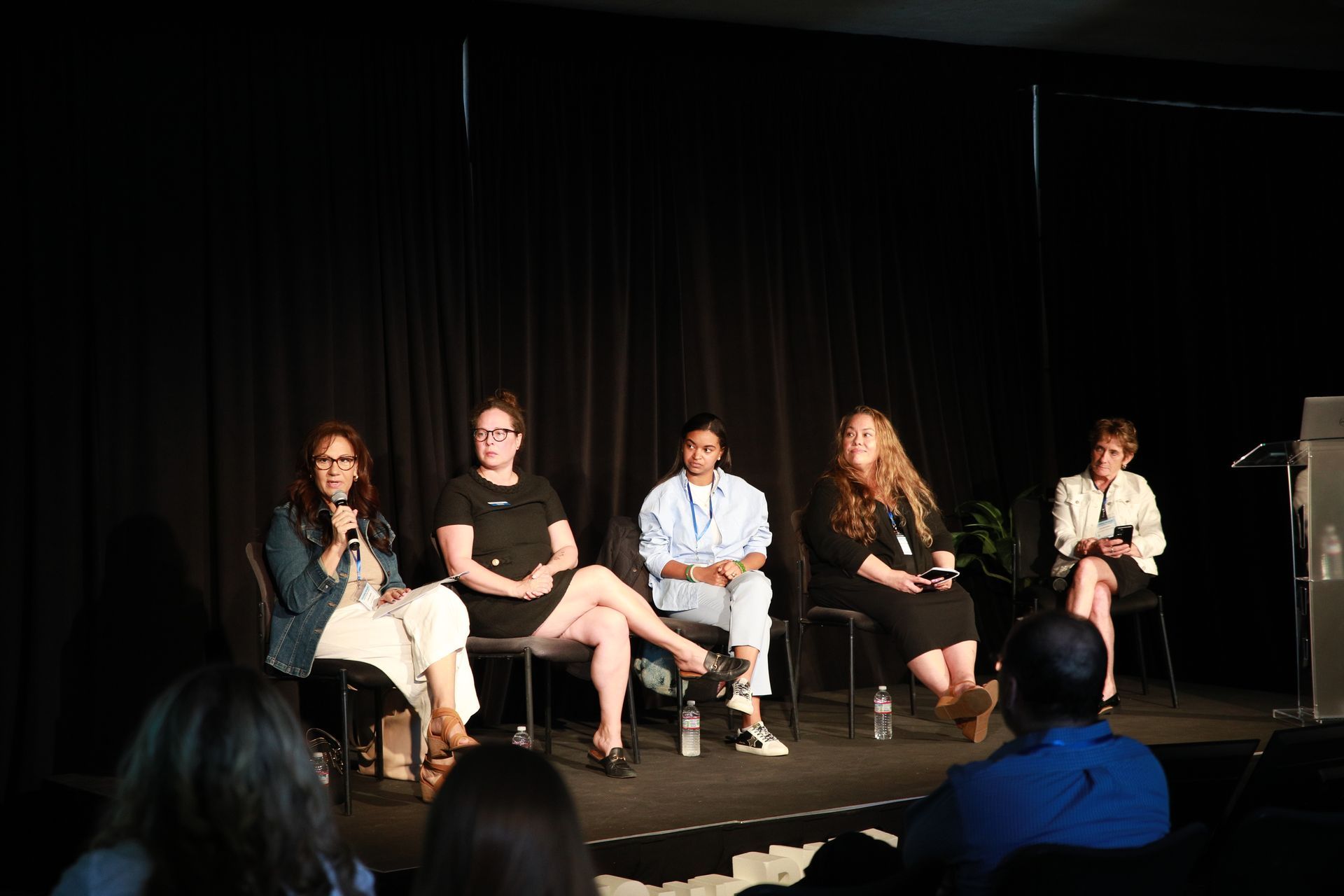 Five panelists seated on stage during a discussion, with audience members in the foreground.