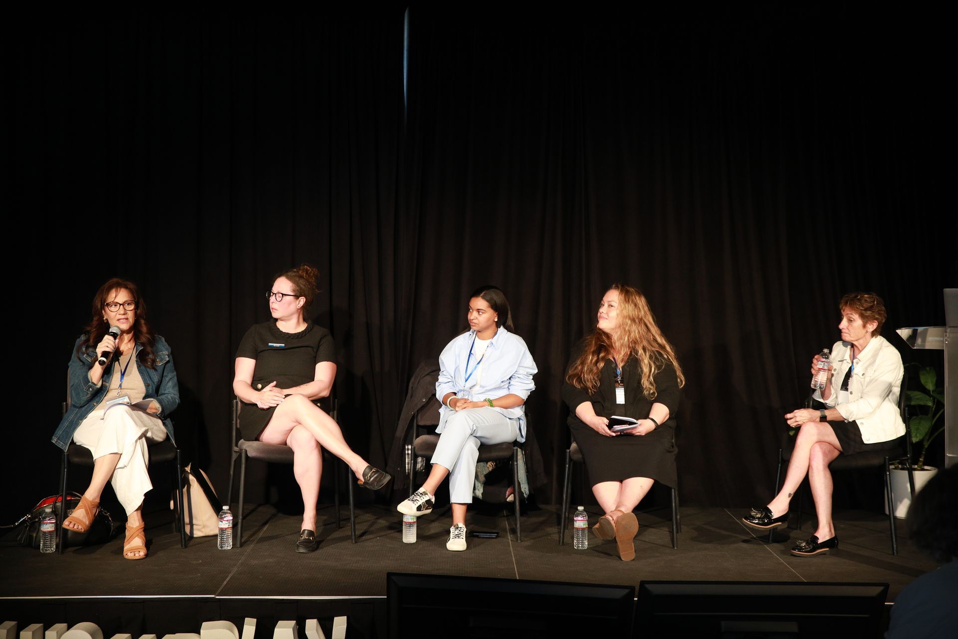 Five people seated on stage in a panel discussion against a black curtain backdrop.