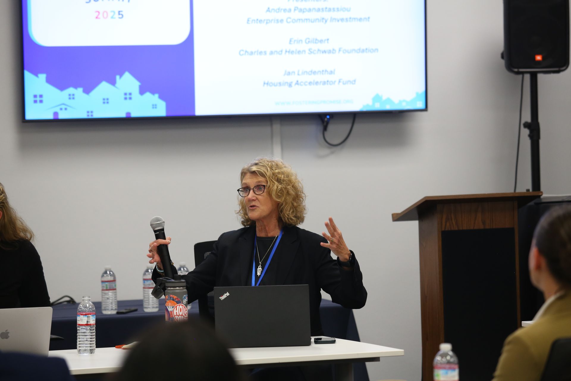 Woman speaking into a microphone at a conference table during a presentation