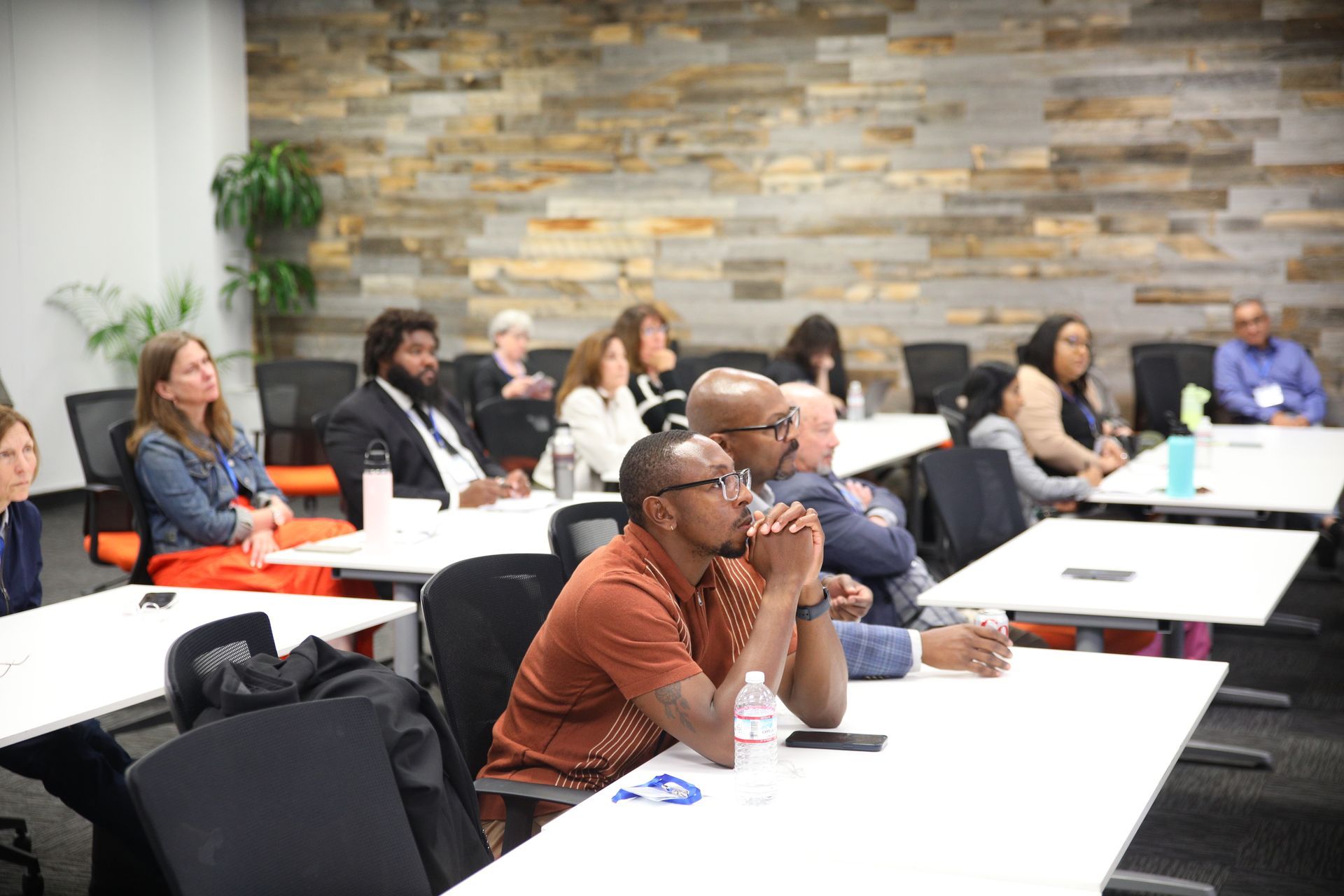 People seated at tables in a classroom or workshop, listening attentively in a modern meeting room.