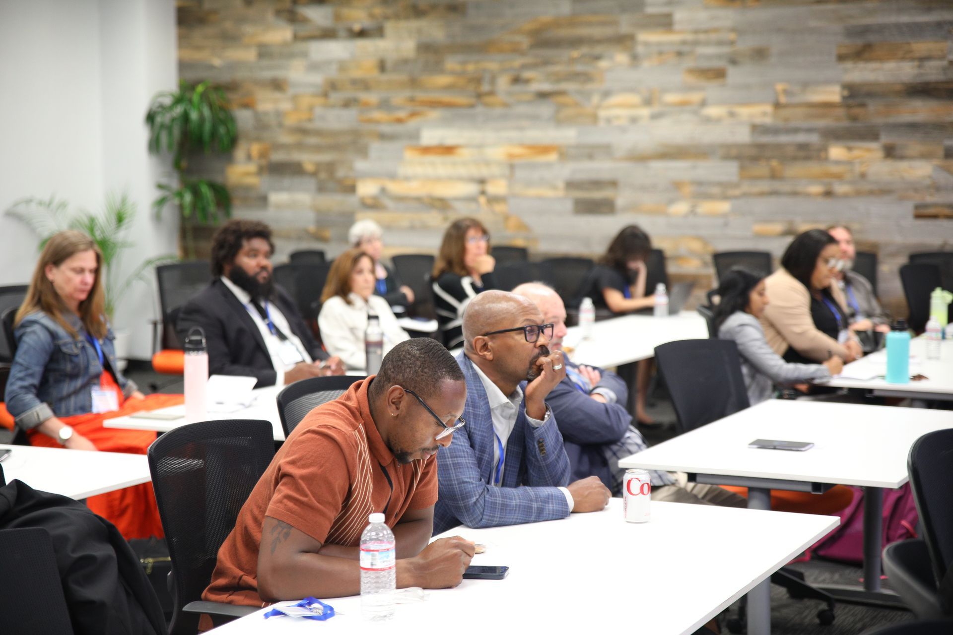 People seated at tables in a classroom or workshop, taking notes during a presentation.