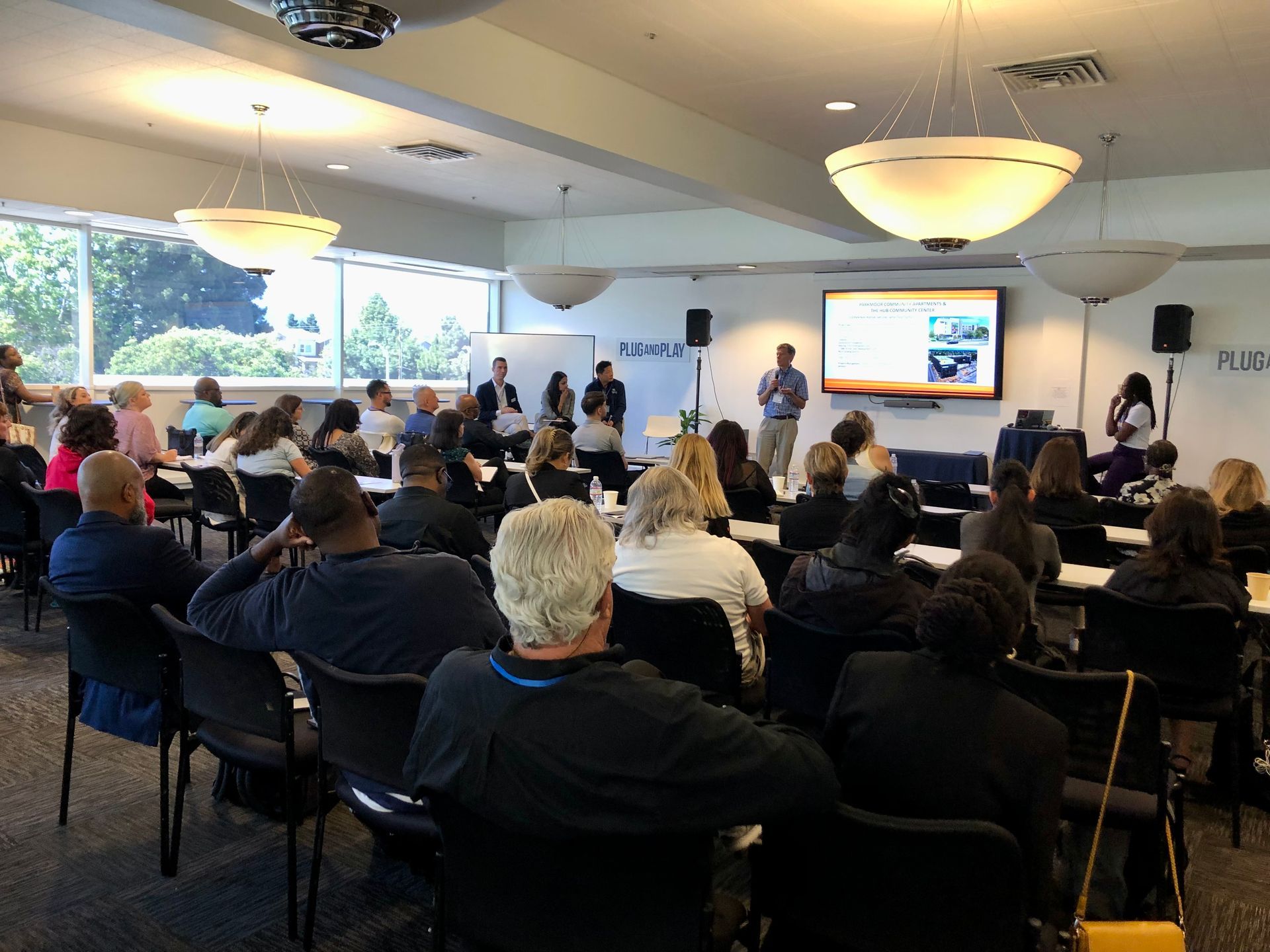 Audience seated in a conference room watching a presentation on a large screen.