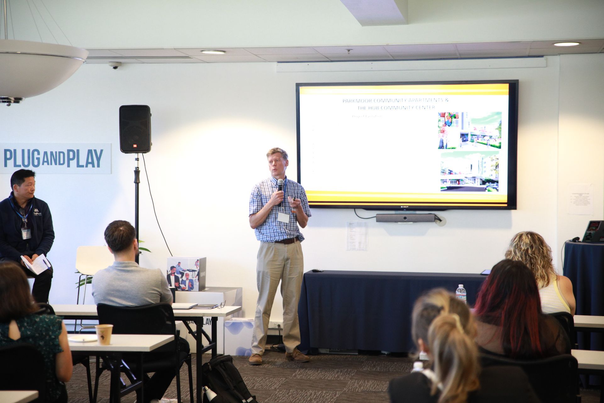 Speaker presenting to an audience in a conference room beside a large projected screen