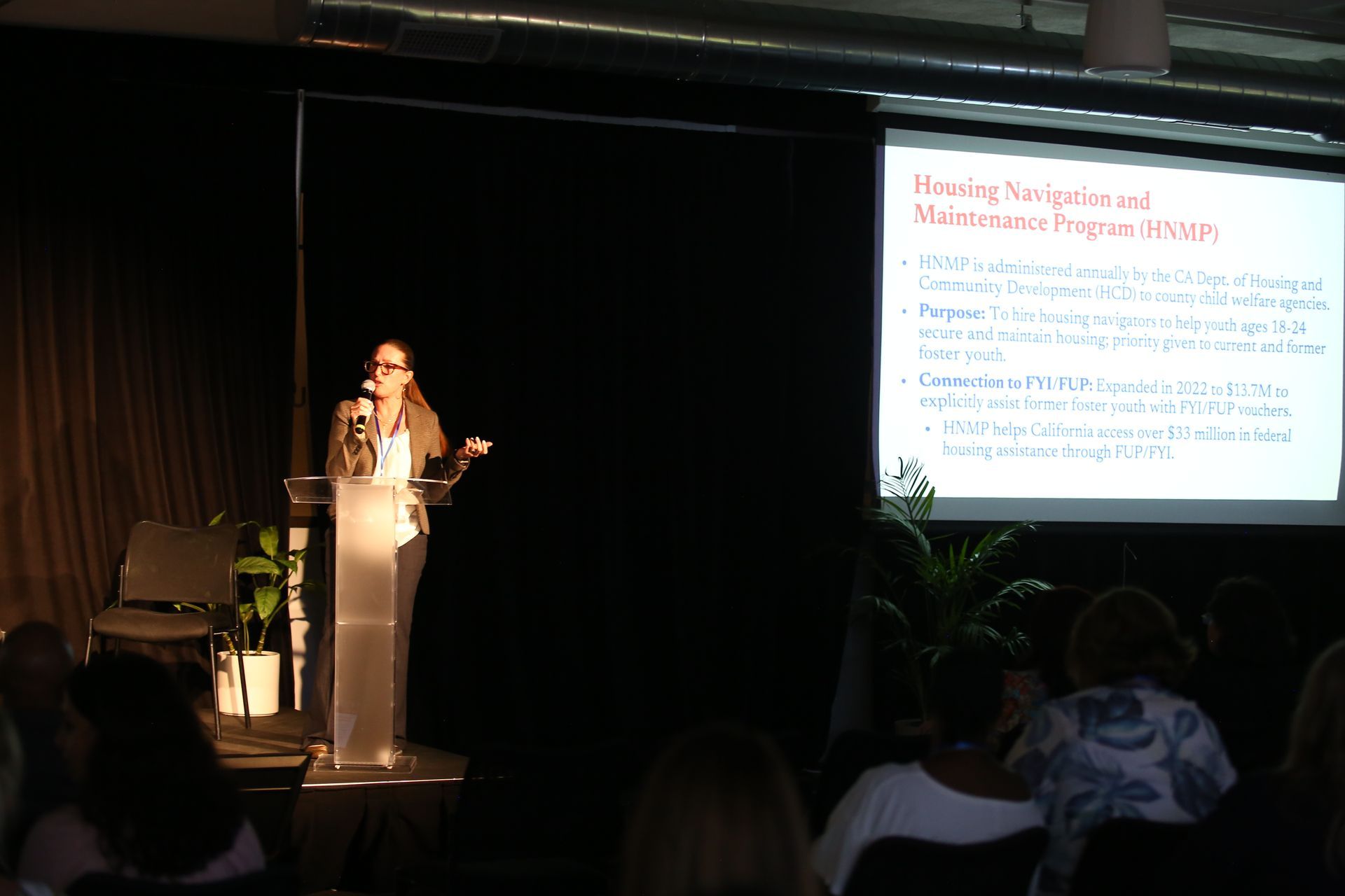 Presenter at podium beside projected slide during a conference talk