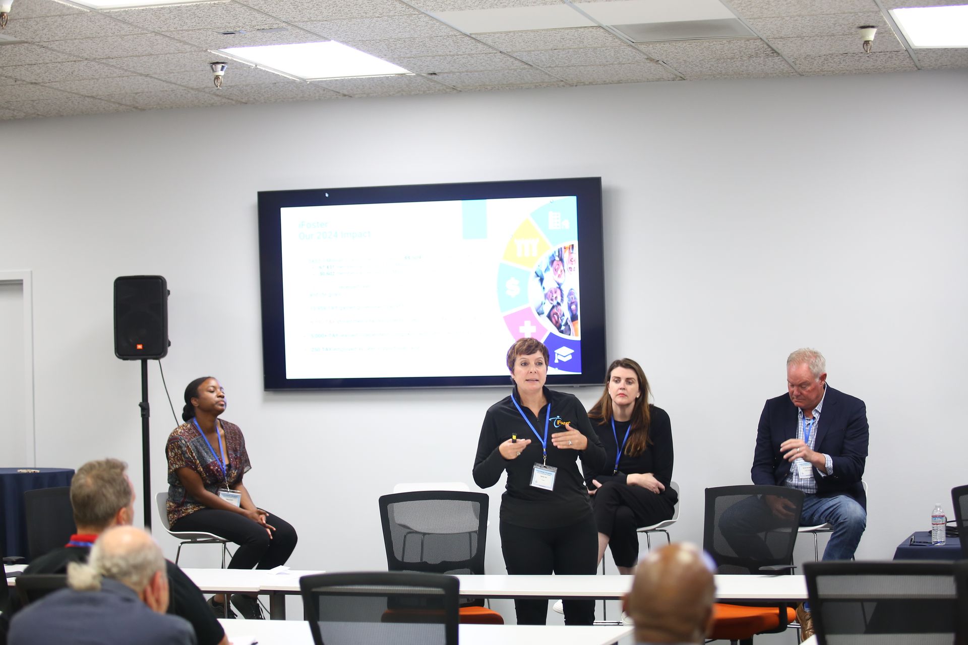 Panel discussion in a conference room with four speakers seated on stage and an audience facing them.
