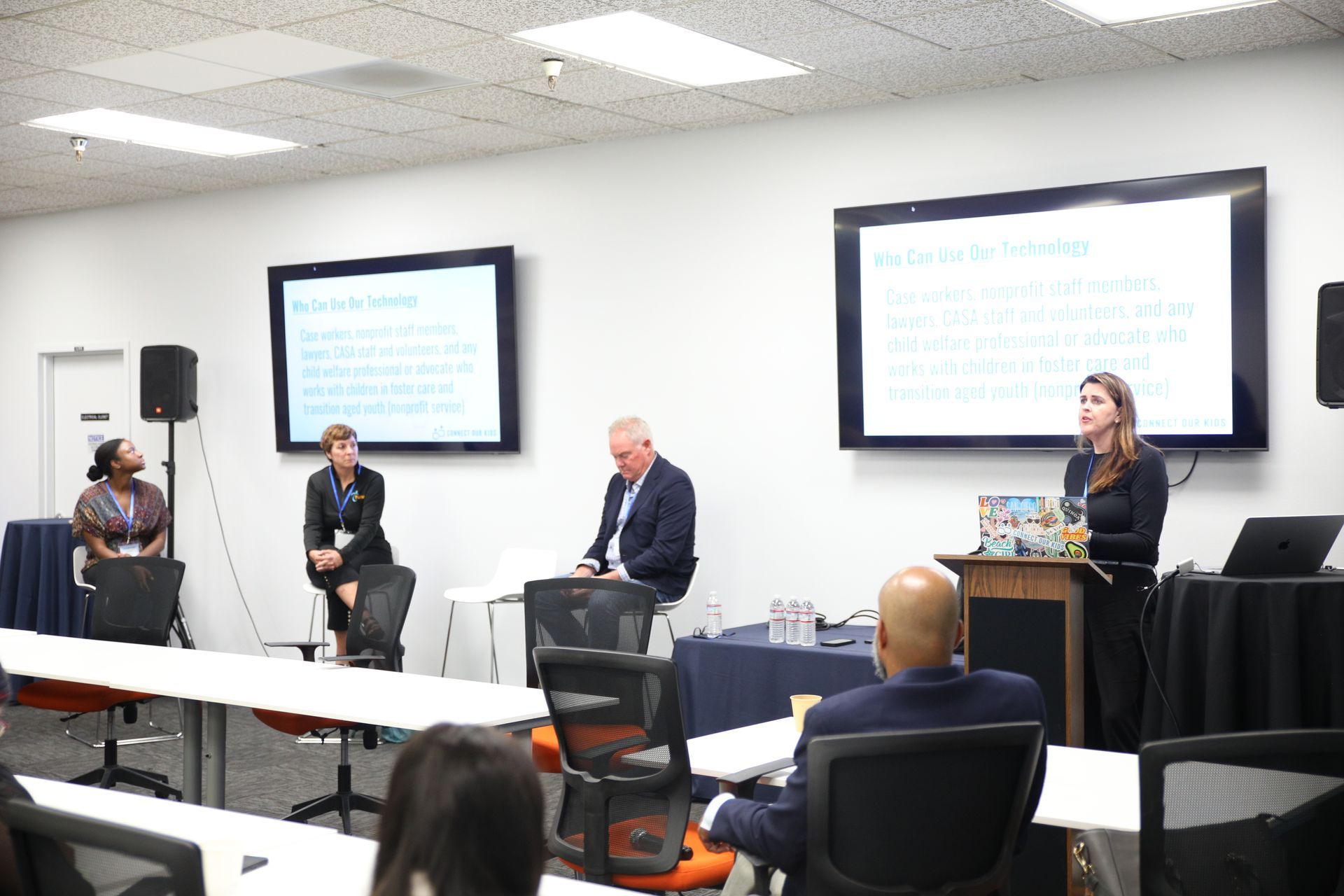 Panel discussion in a classroom with four speakers seated and standing at the front, facing an audience.