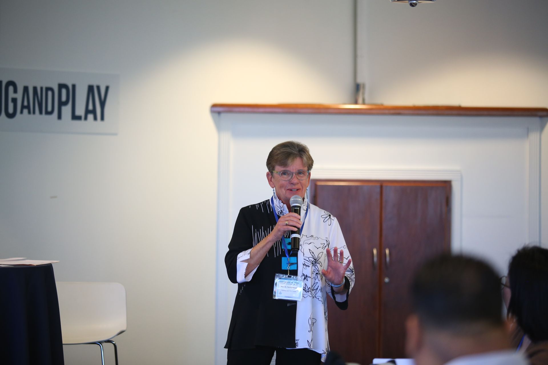 Speaker holding a microphone at a conference podium, standing before a small audience.