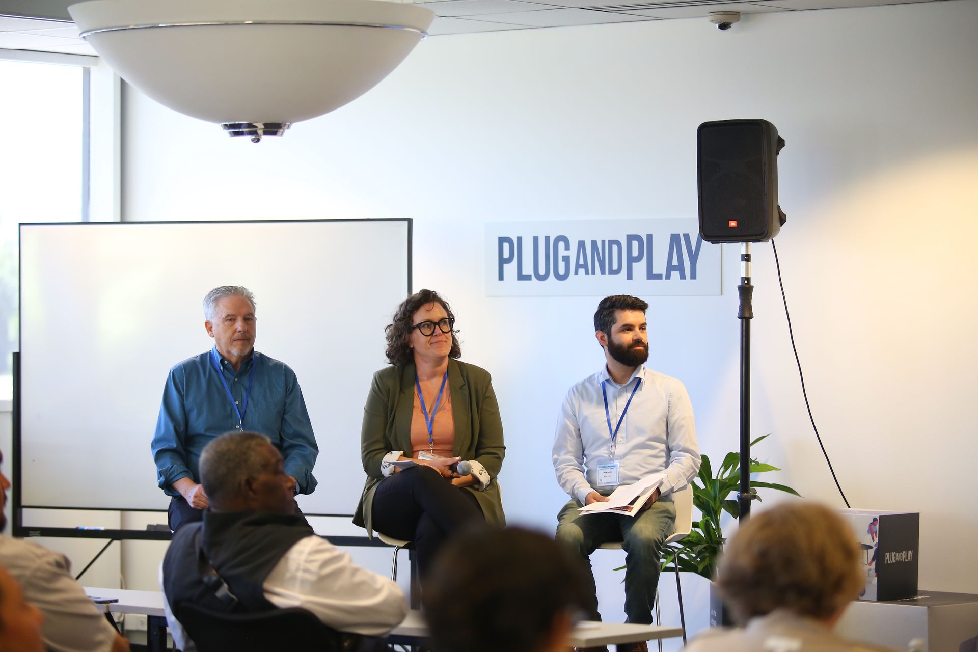 Panel discussion on stage with three speakers seated before a Plug and Play backdrop