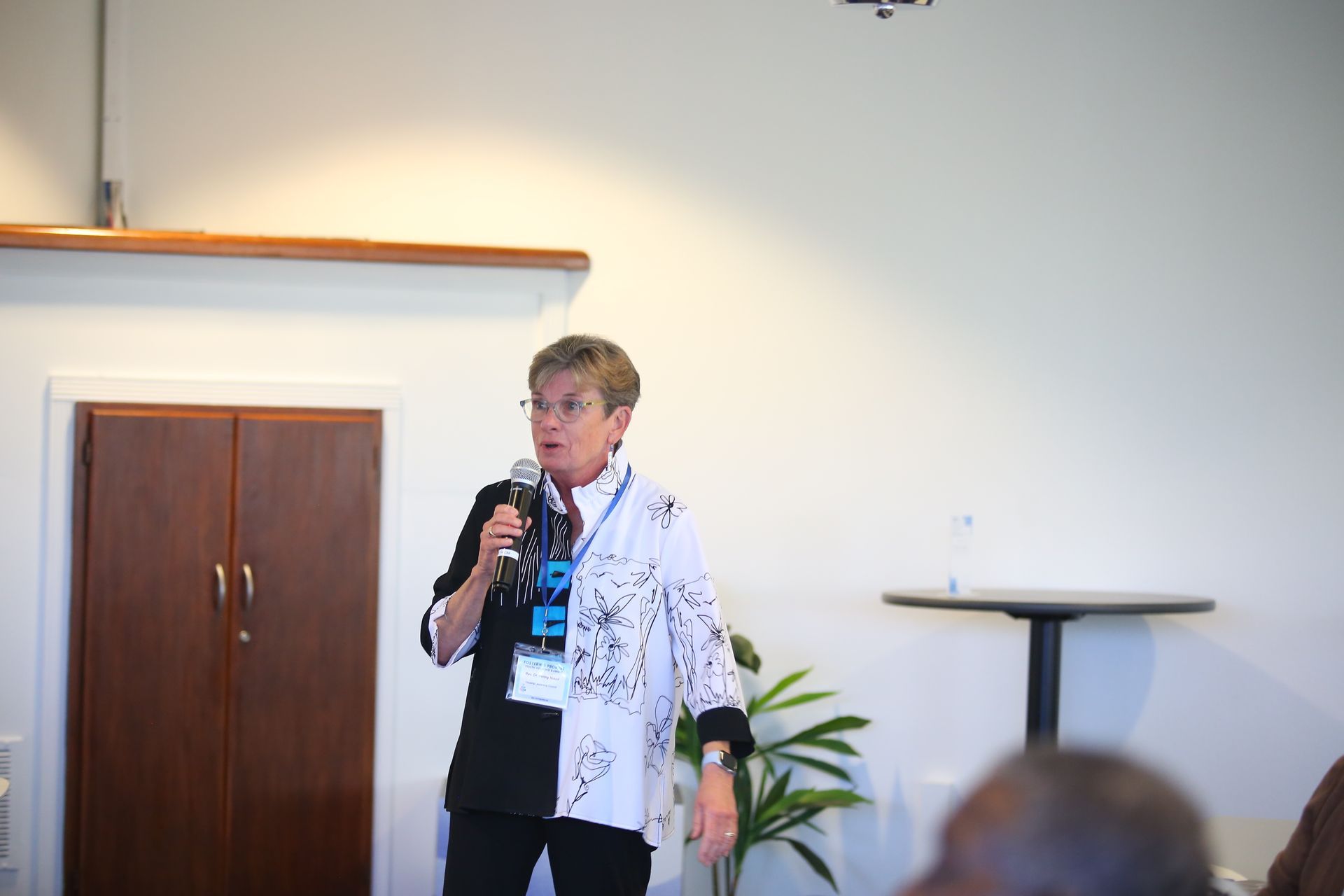 Person speaking into a microphone beside a podium in a conference room.