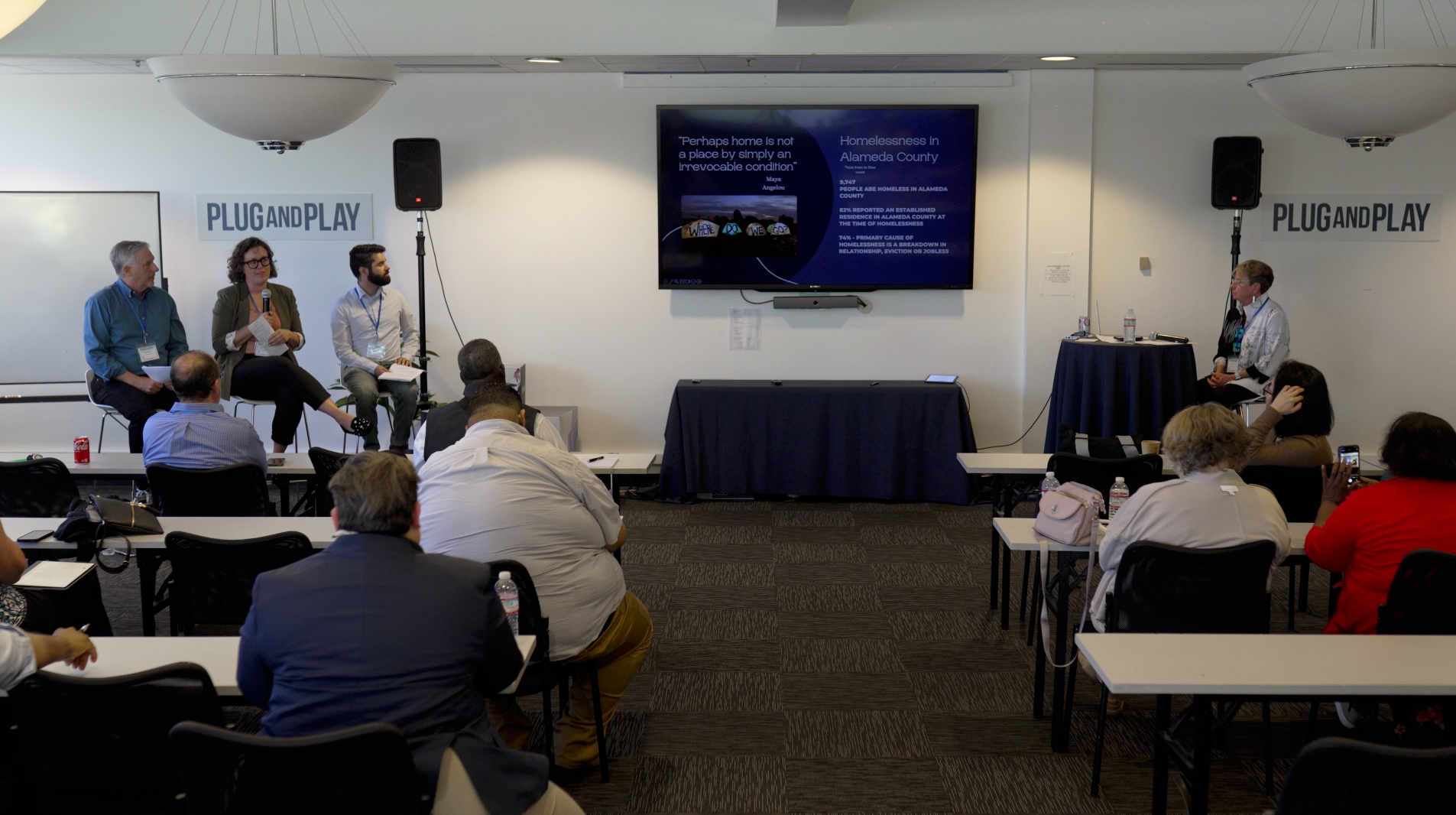 Panel discussion in a conference room, with speakers on stage and audience seated at tables.
