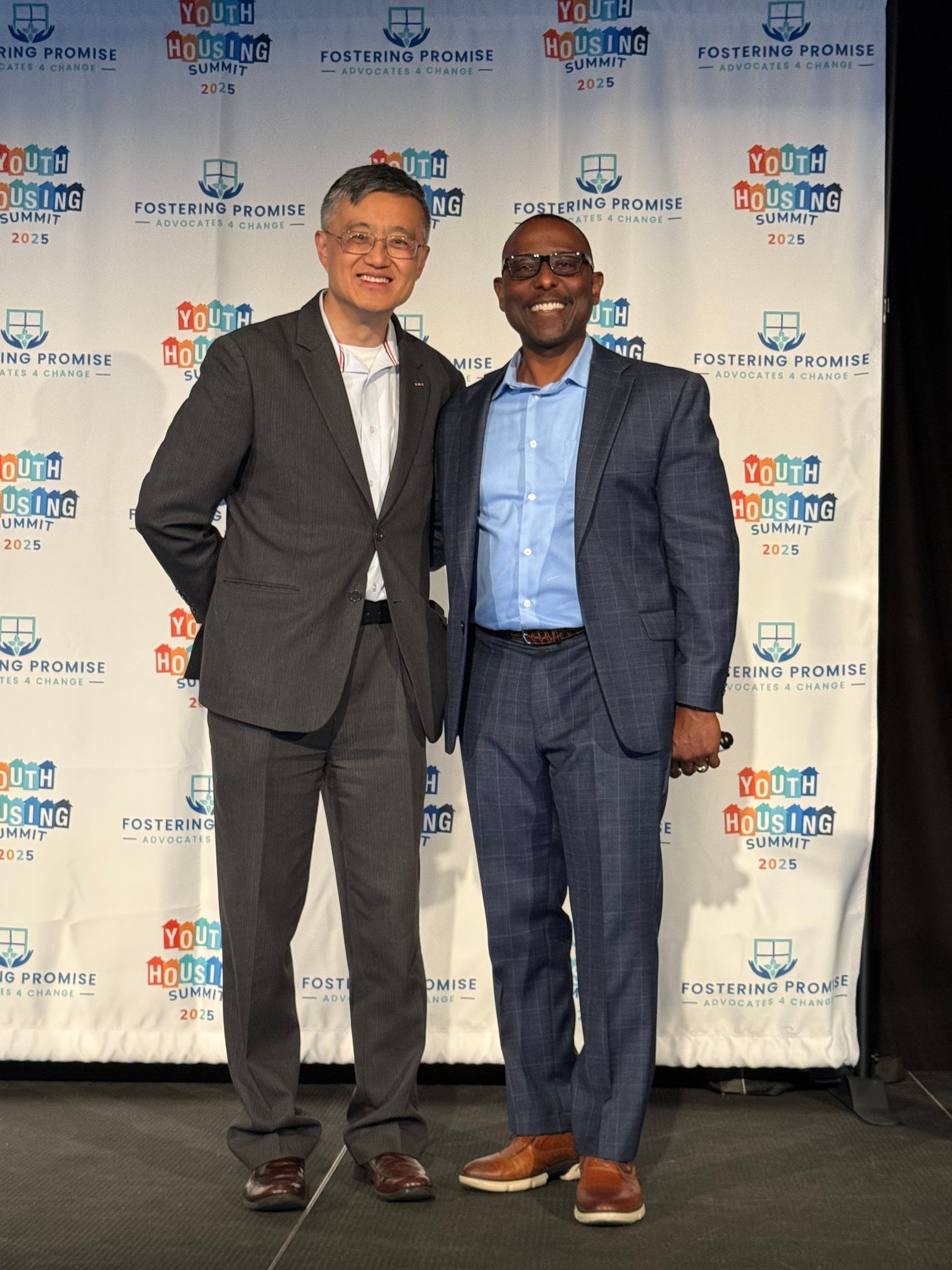 Two men in suits smiling at a step-and-repeat event backdrop