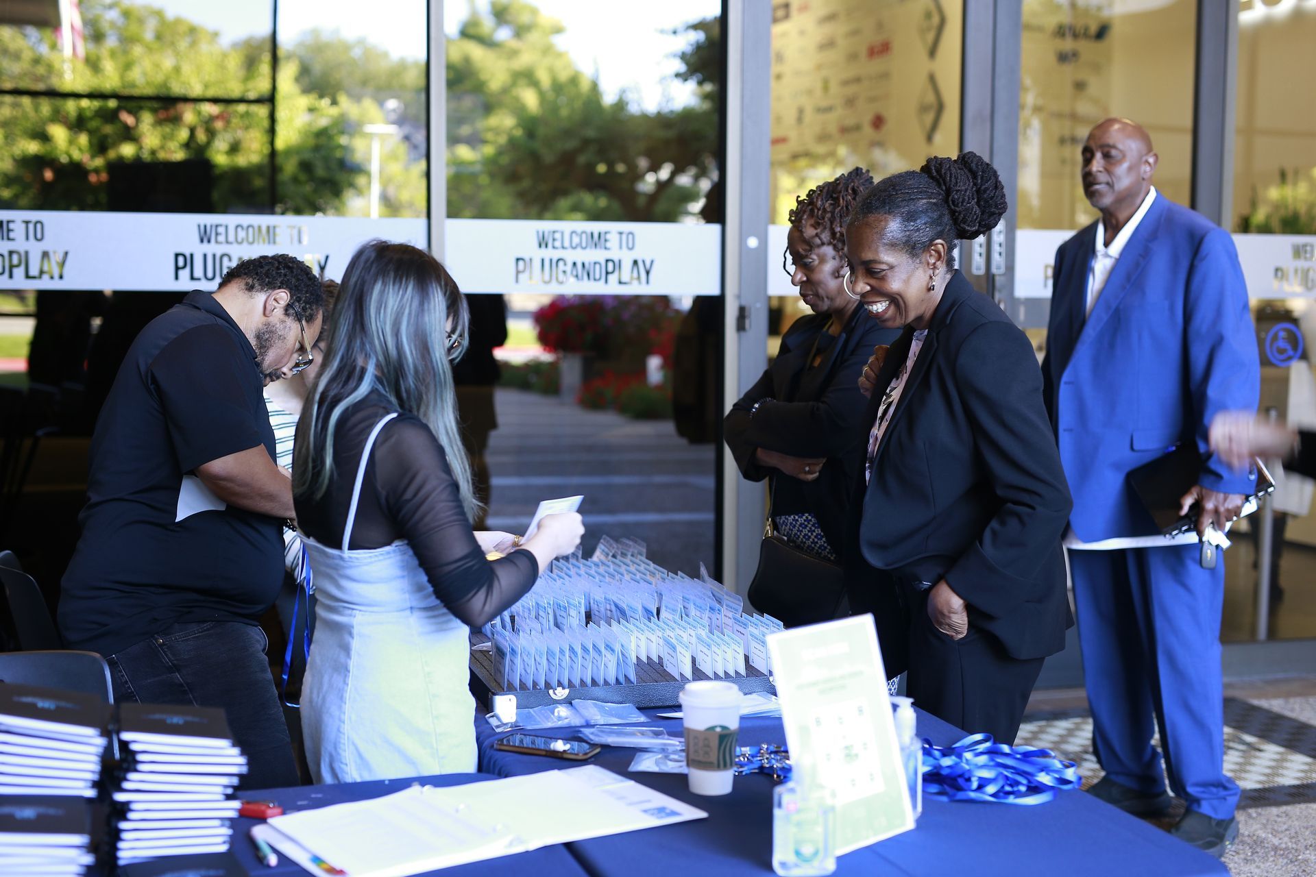 People at a blue table signing in at an outdoor event, with water bottles and papers displayed