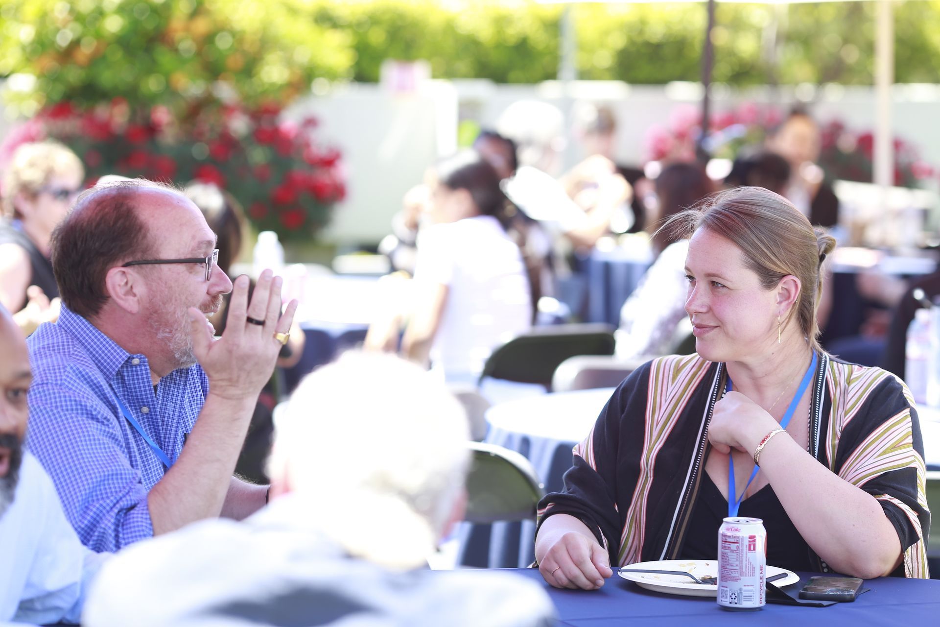 Two people talking at an outdoor table with drinks in a sunny garden setting