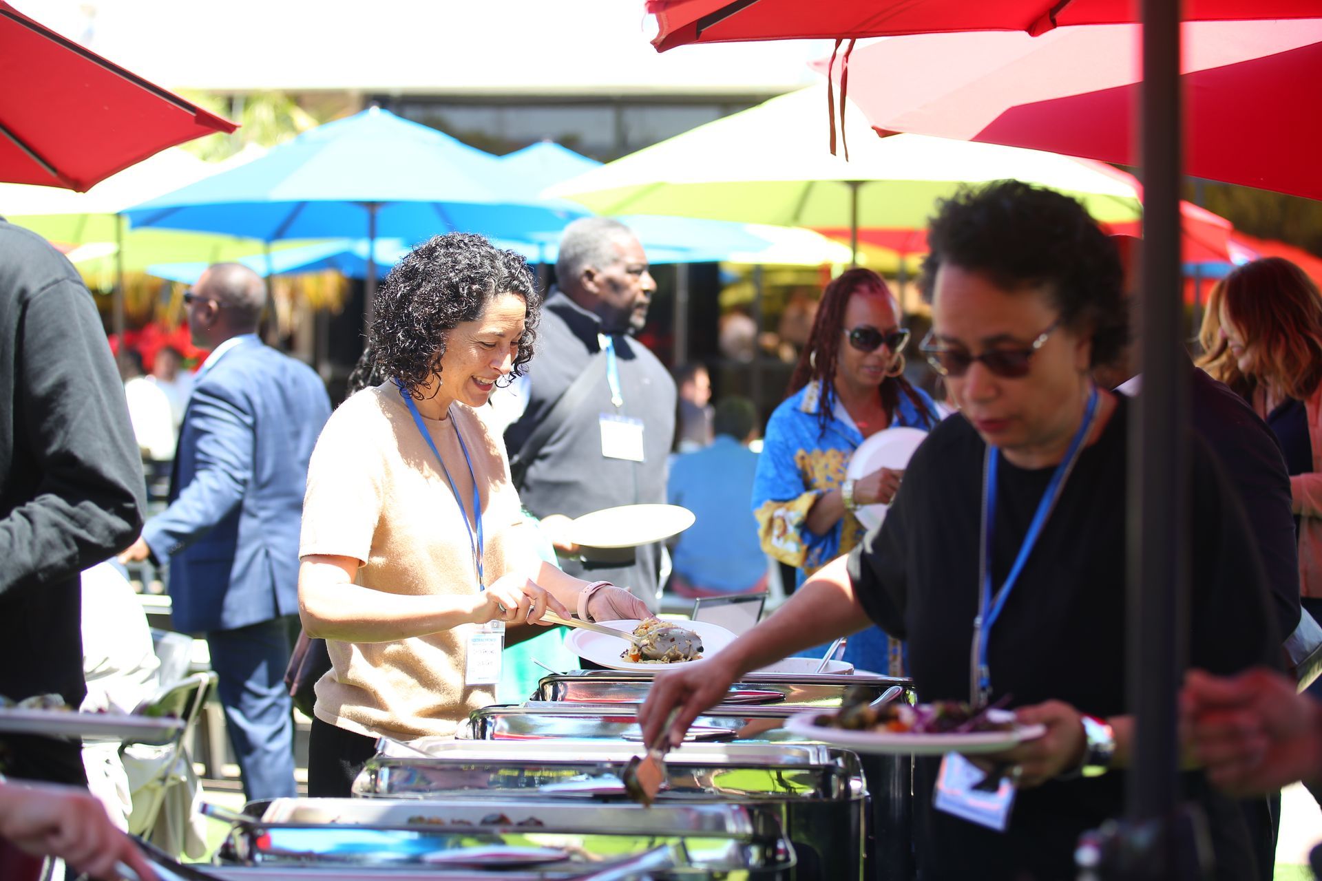 People browsing trays of food at an outdoor market under colorful umbrellas