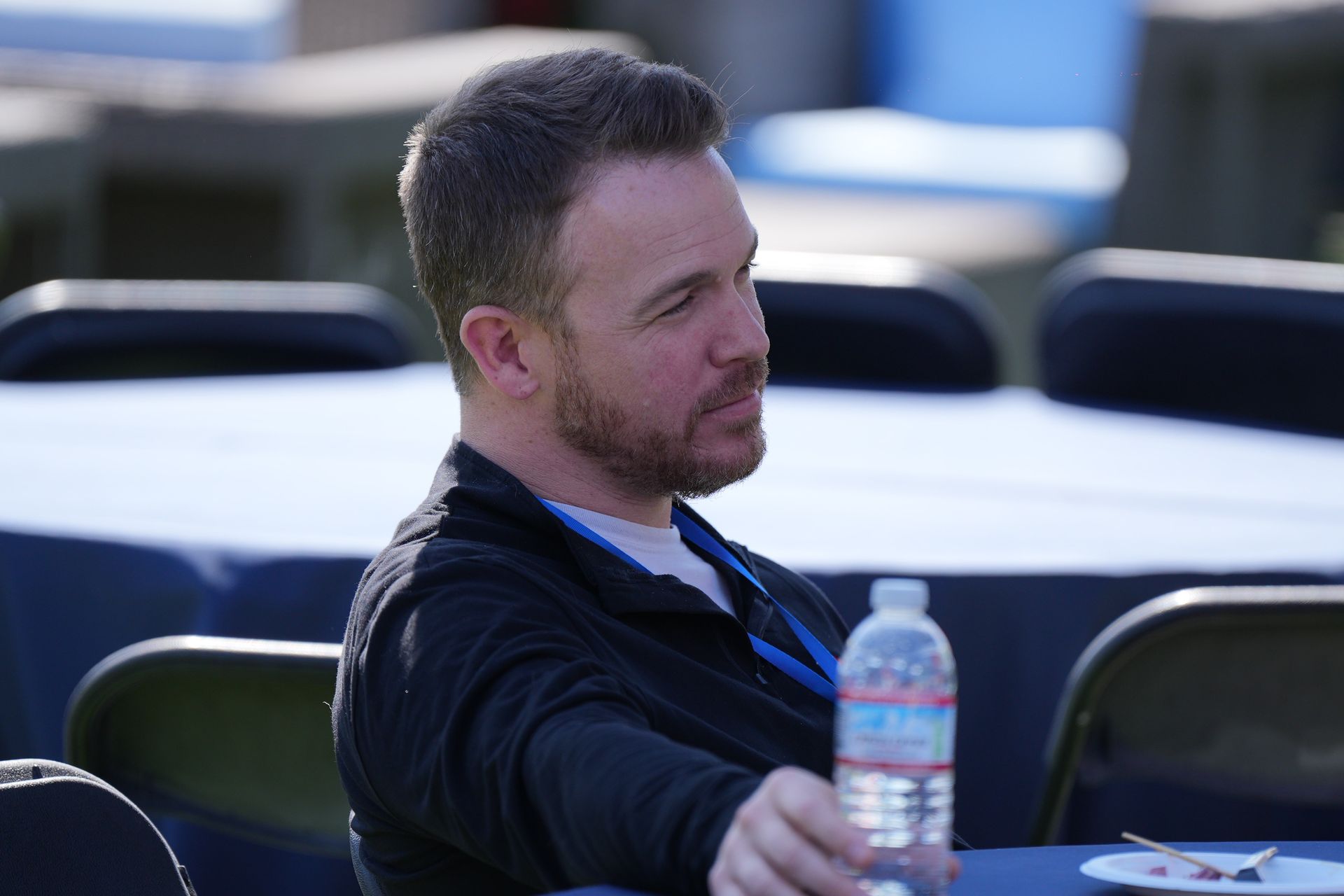 Man seated outdoors holding a water bottle, wearing a dark jacket and looking to the side