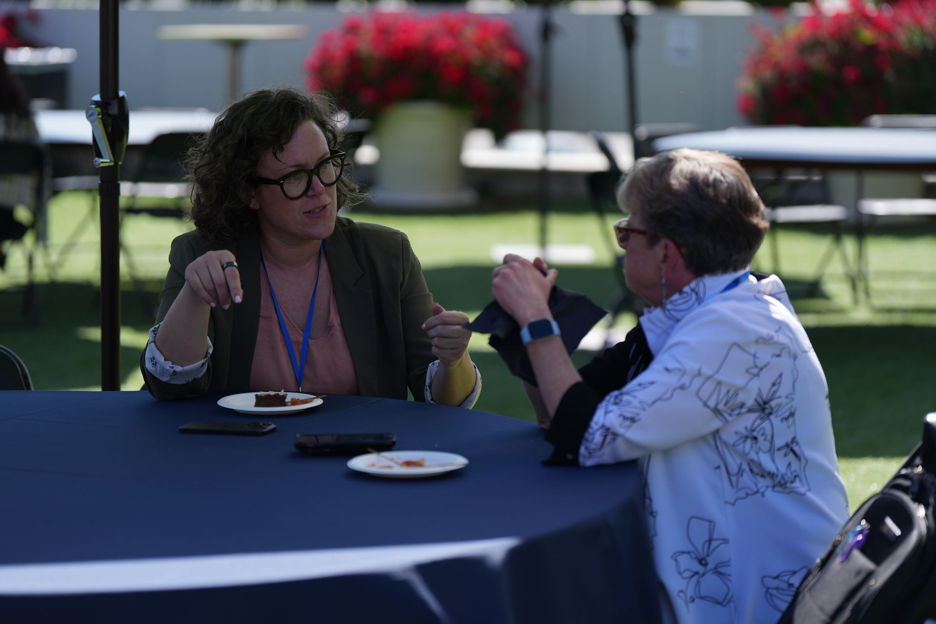 Two people talking at a table outdoors, with drinks and plates in a sunny garden setting