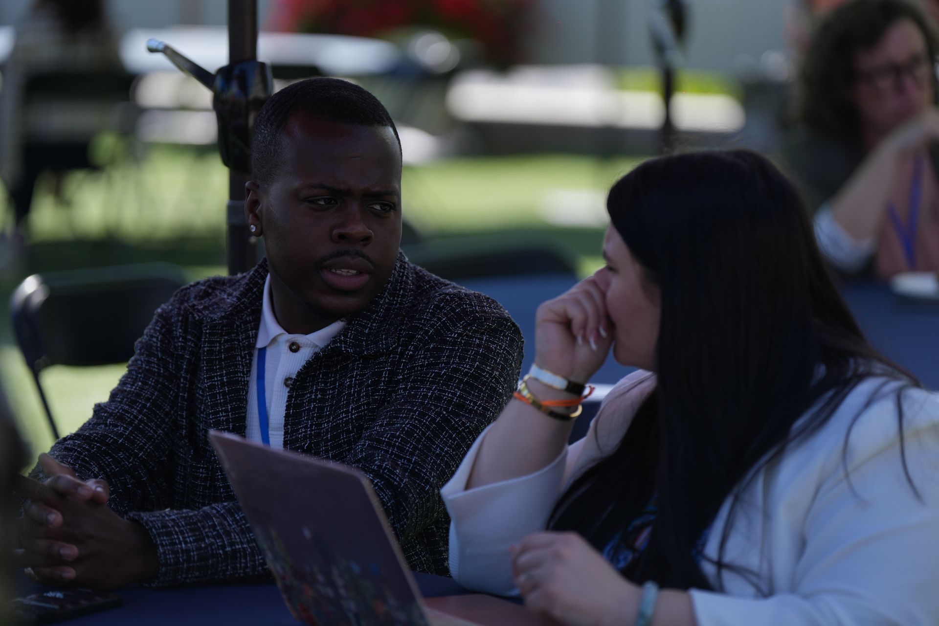 Two people talking at an outdoor table with a laptop in front of them