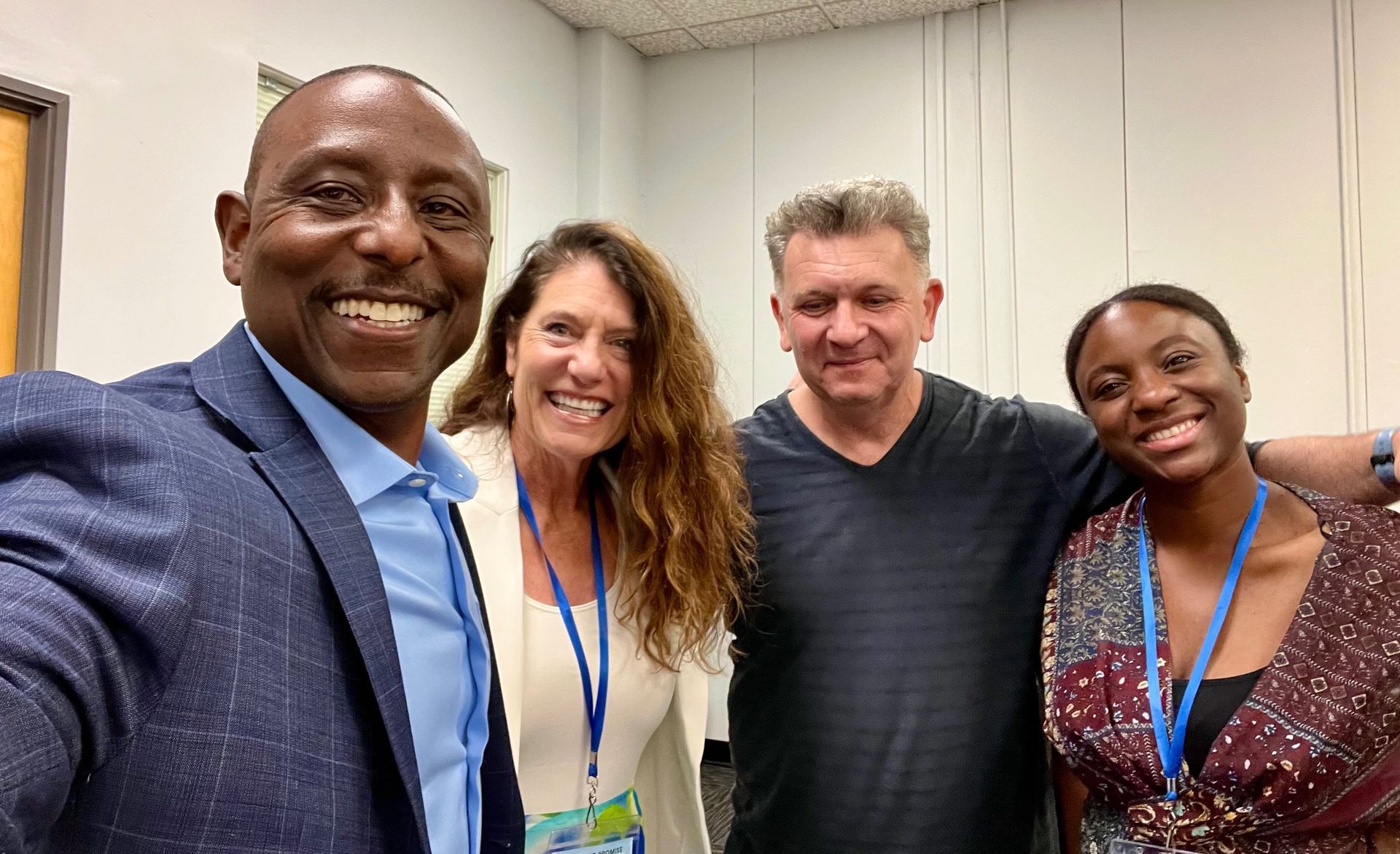 Four smiling coworkers posing indoors with blue lanyards at a conference.