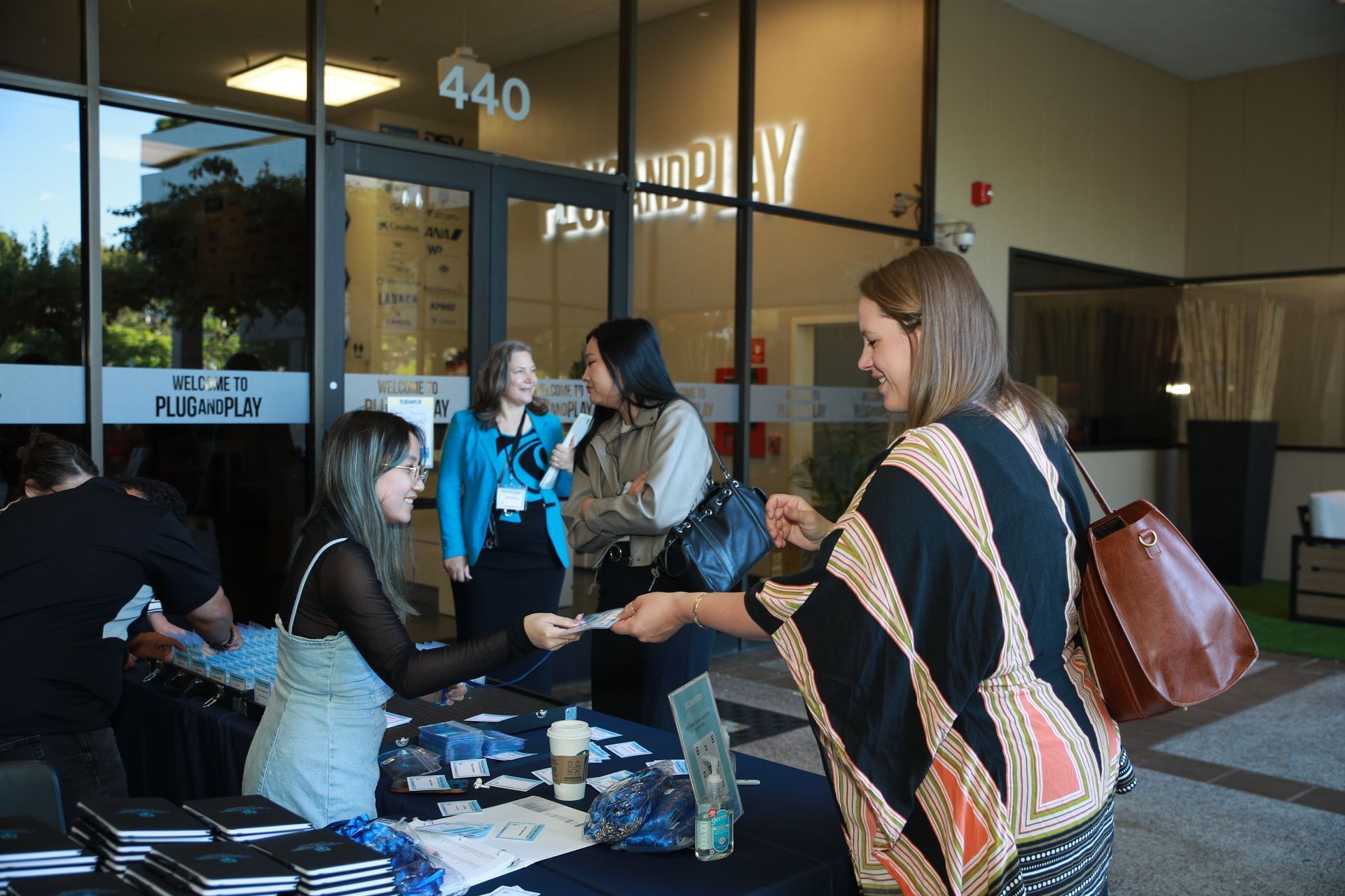 People signing in at a table outside a glass-fronted building with “440” above the entrance