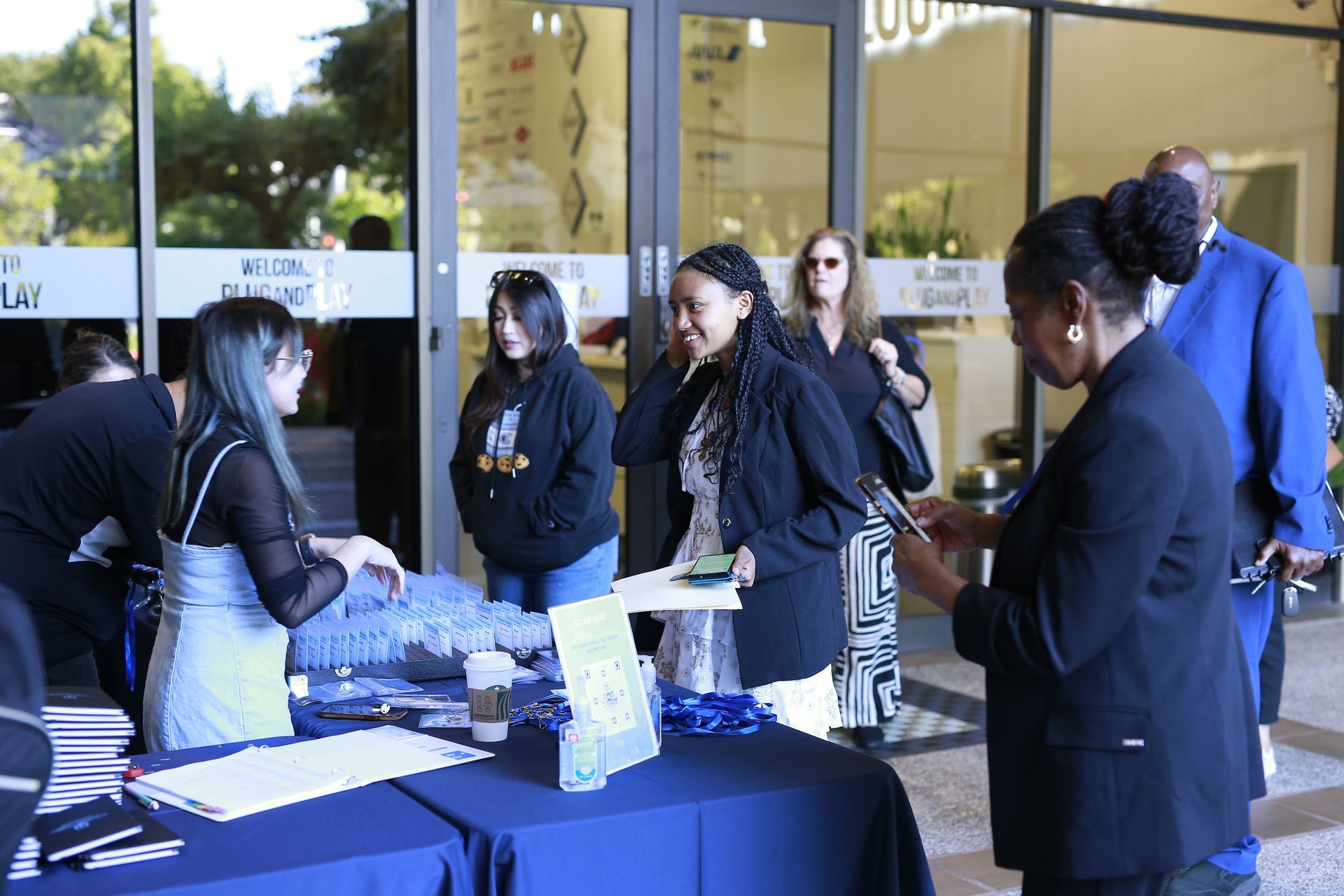 People gathered at an outdoor registration table, talking and handling papers near a building entrance.