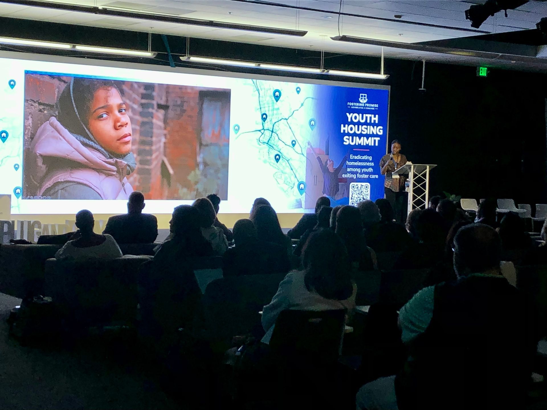 Audience watching a youth housing summit presentation on a large stage screen