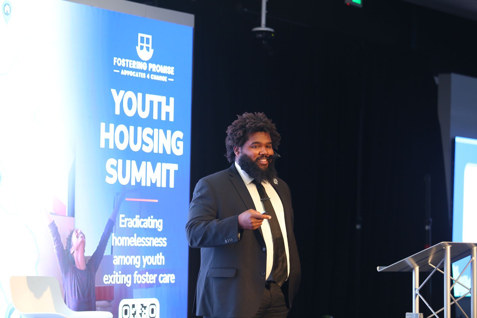 Speaker at Youth Housing Summit podium beside blue event banner