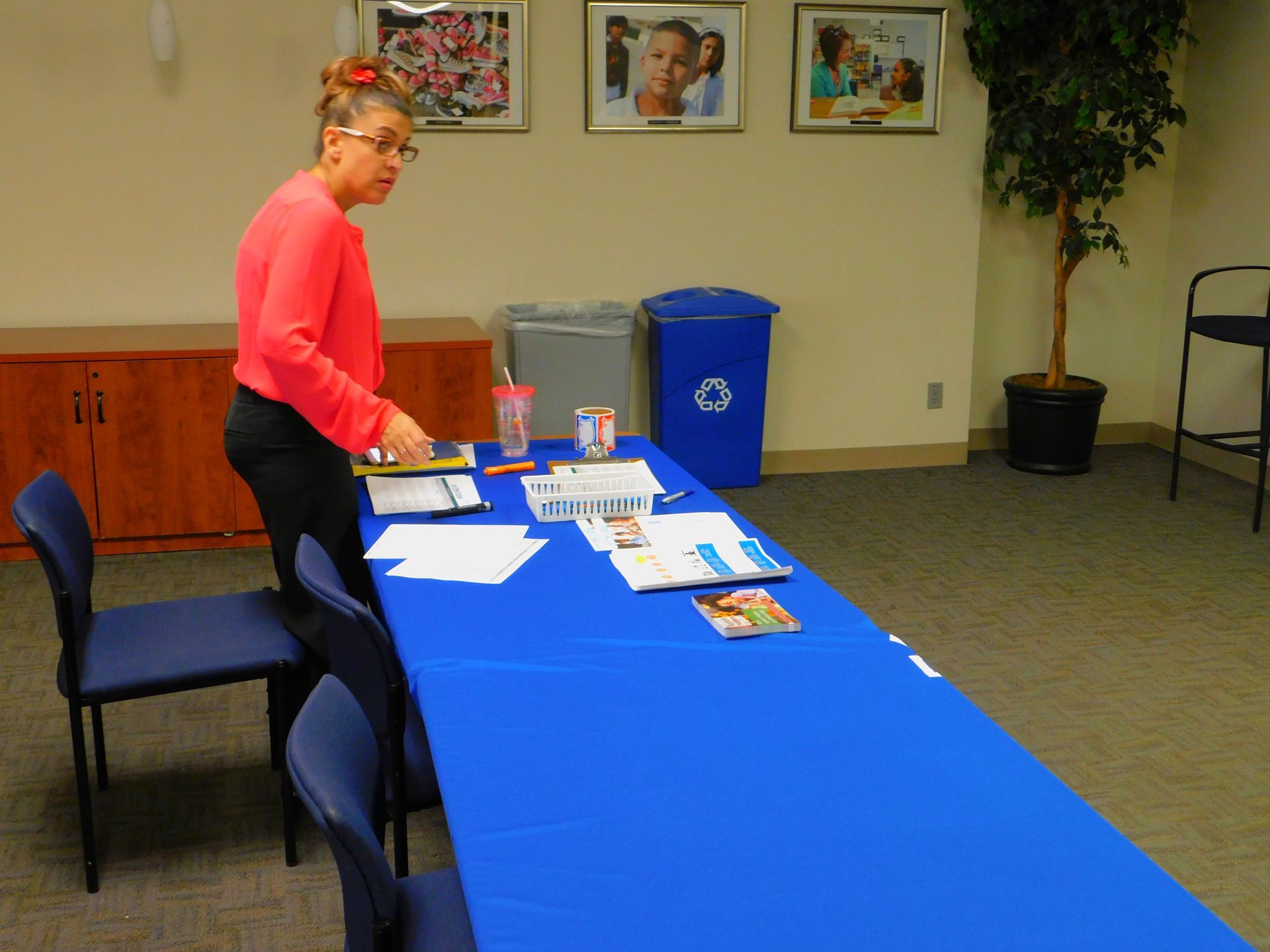 Person standing by a blue-covered table with papers and drinks in a community room