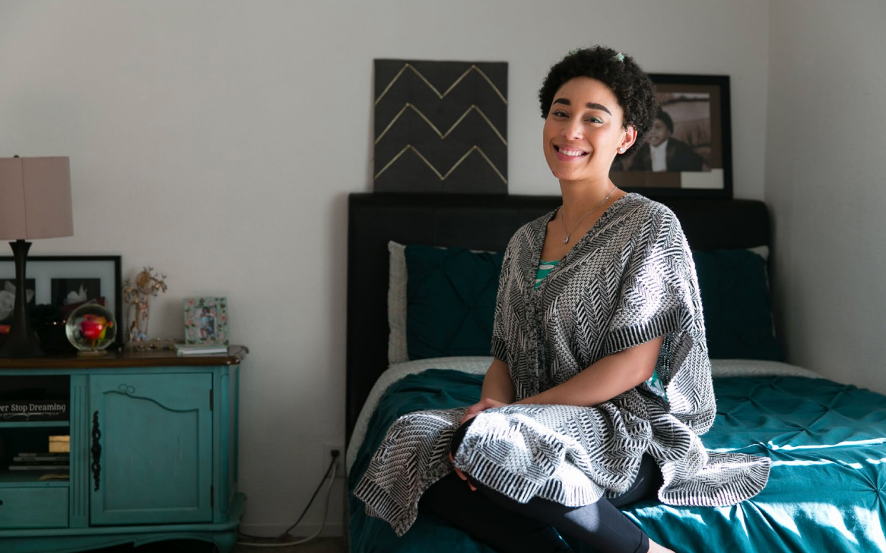 Person sitting on a bed in a teal bedroom, smiling at the camera.