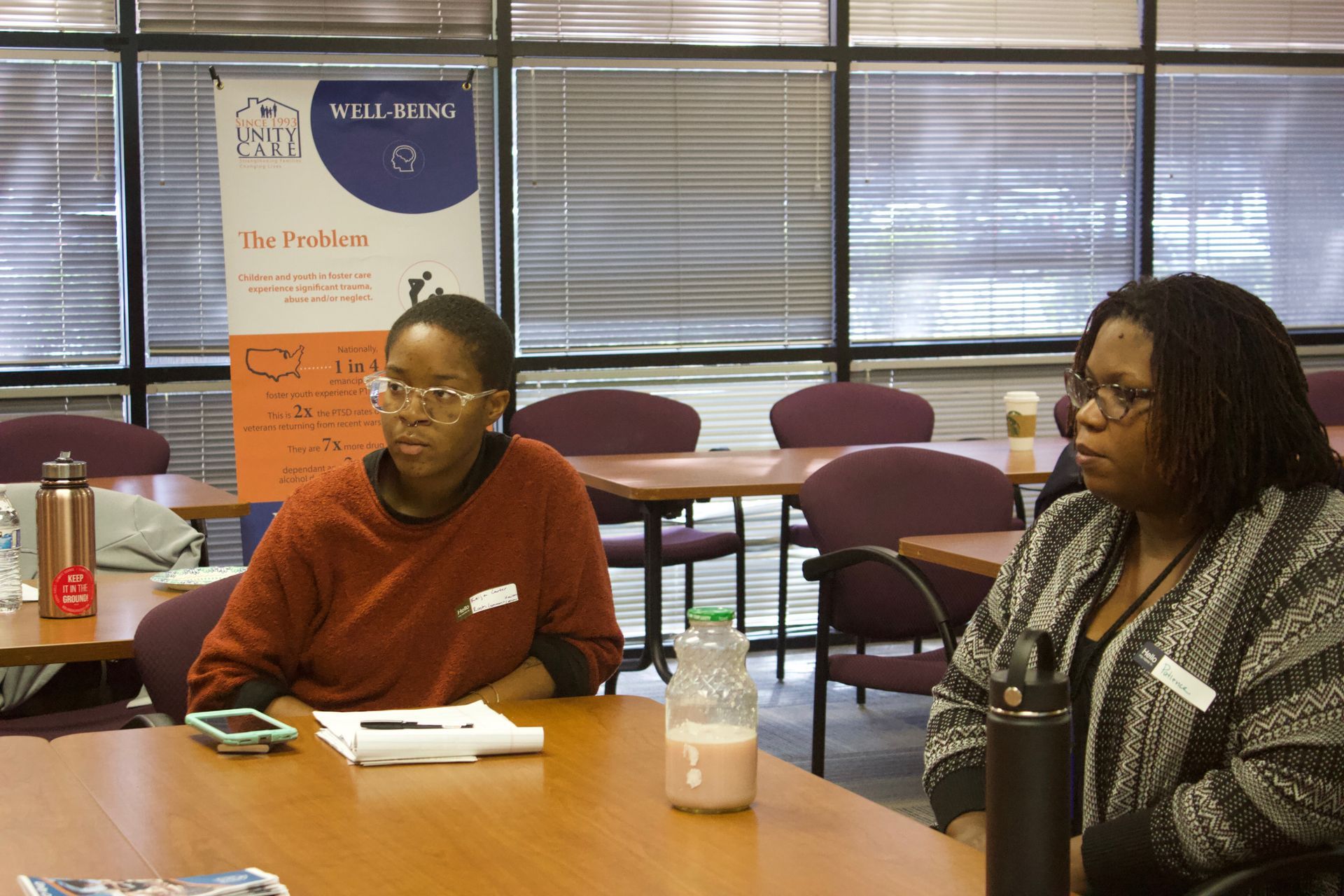 Two people seated at a table in a meeting room, listening attentively.