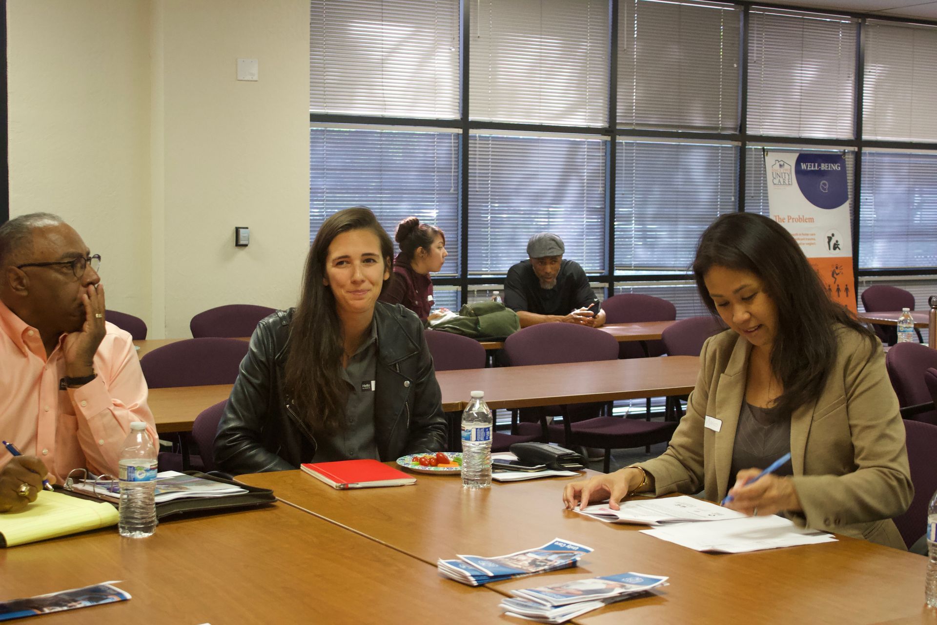 Three people seated at a table in a classroom, reviewing papers and notebooks during a meeting.
