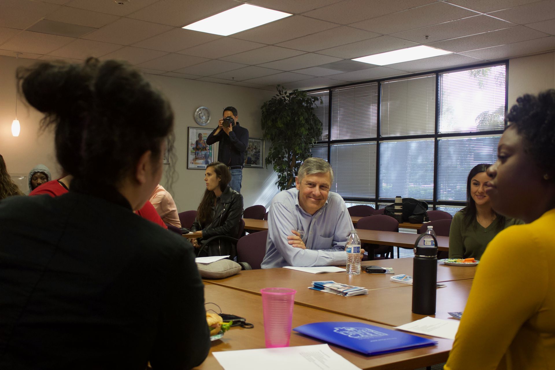People seated around a conference table in a meeting room, with papers, laptops, and a pink cup.