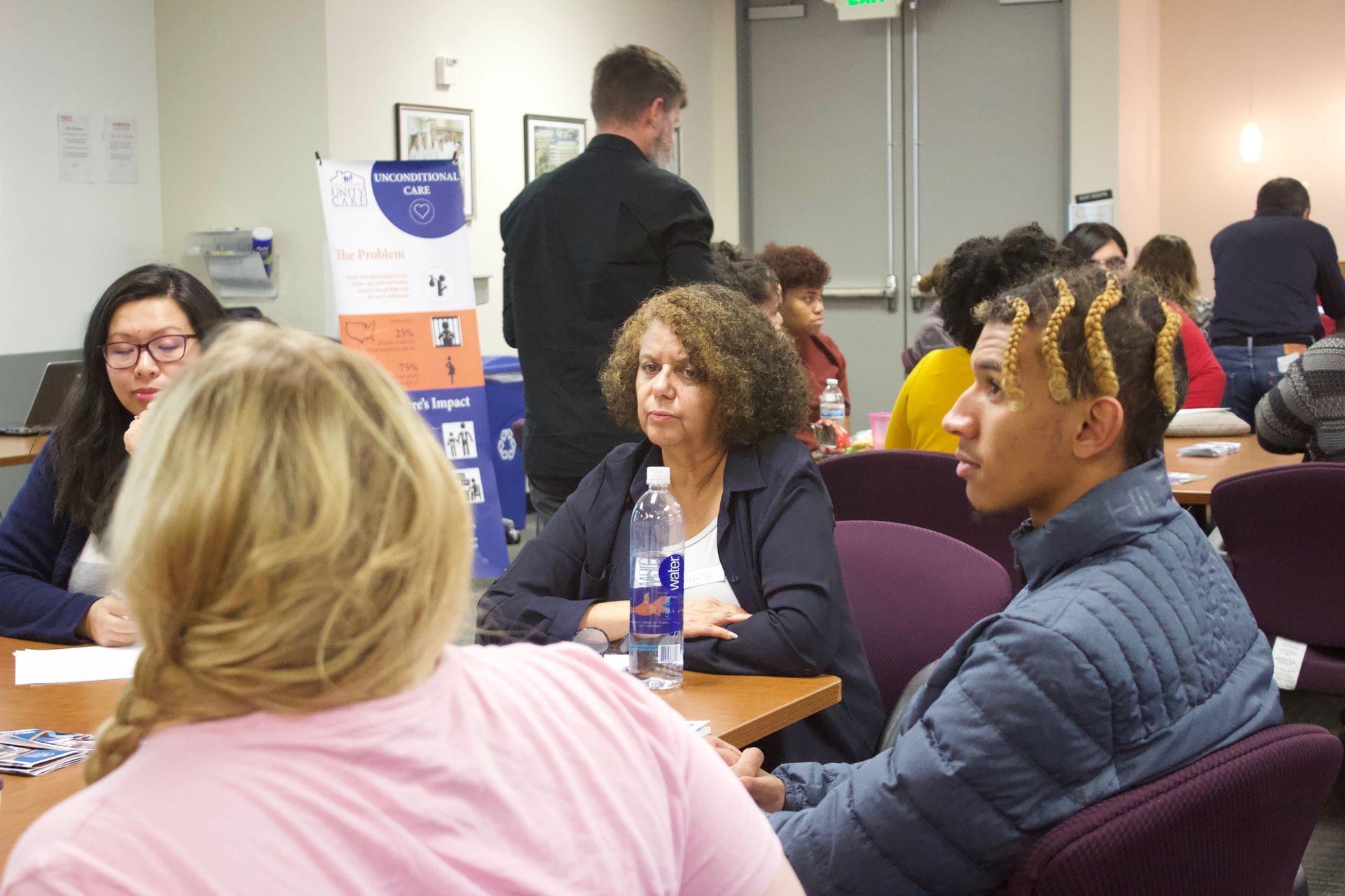 People seated around tables at a workshop, with cups and papers in a conference room.