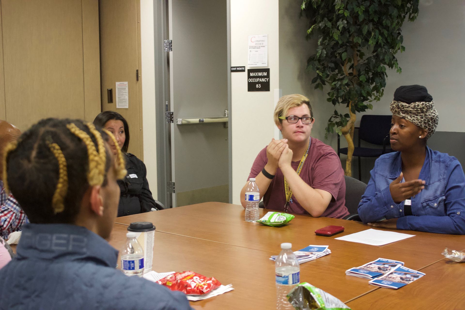 People seated around a conference table in a meeting room, talking with drinks and snacks on the table.
