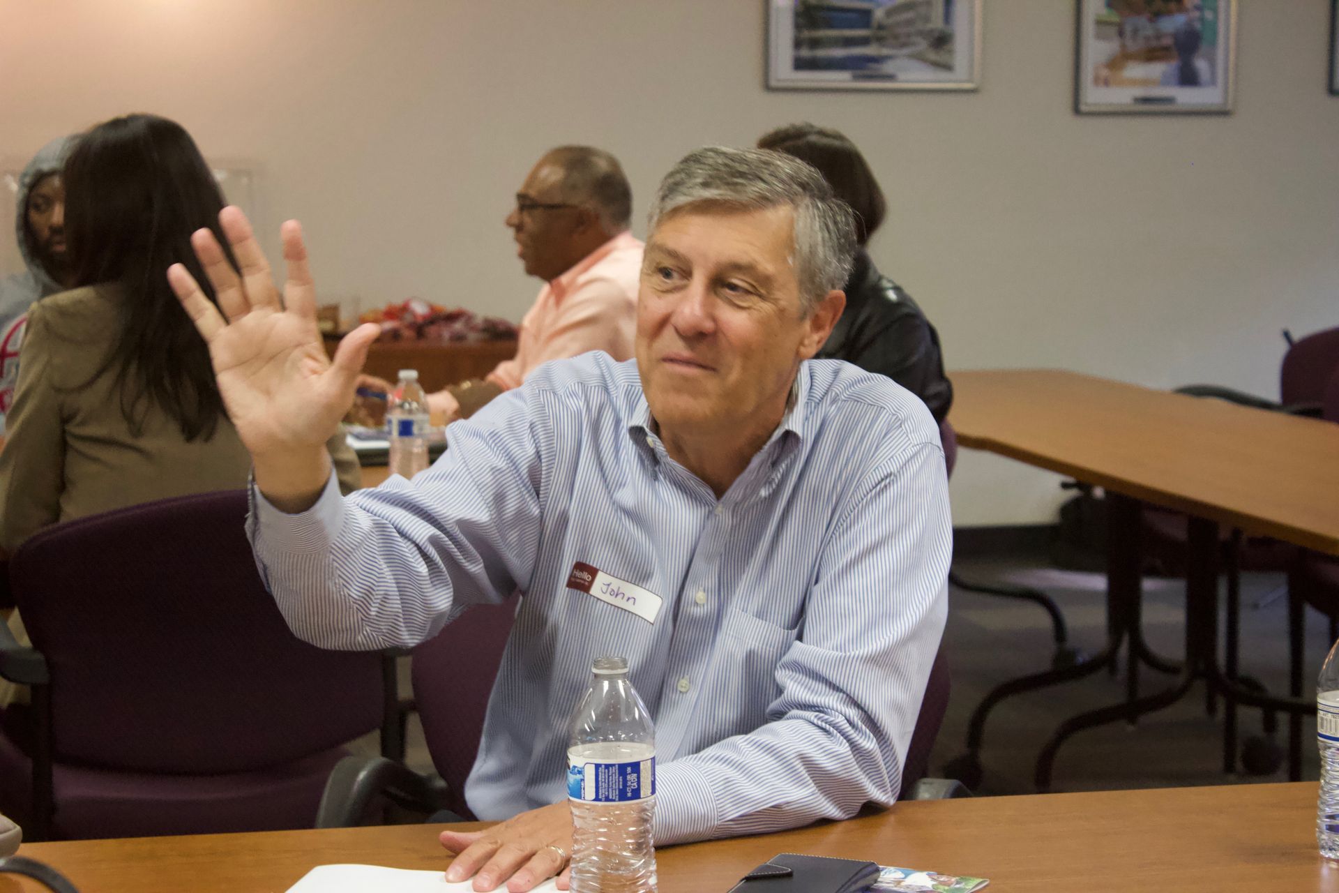 Man in striped shirt raising hand at a meeting table in a conference room