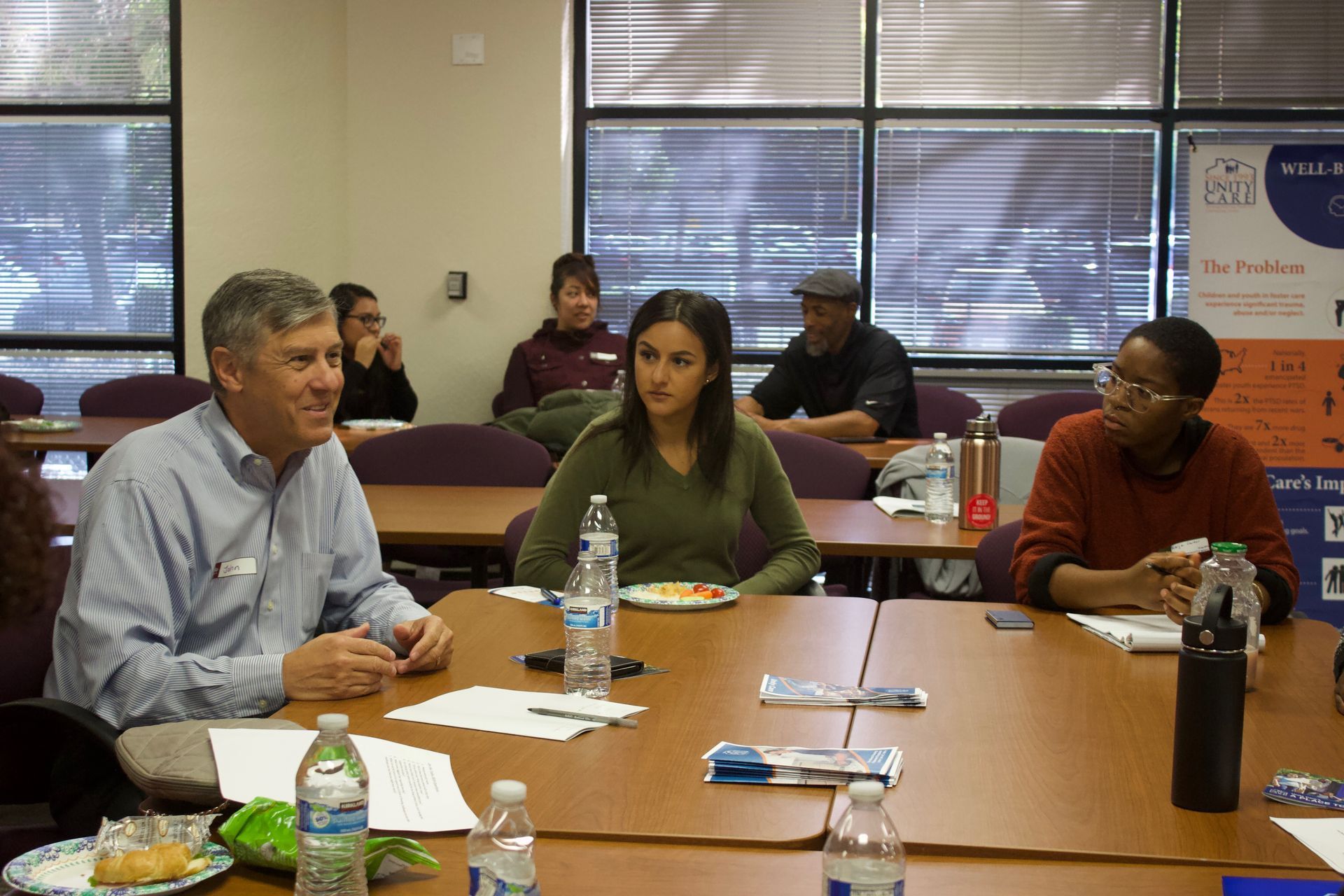 People seated around a conference table in a meeting room, discussing papers and drinks.