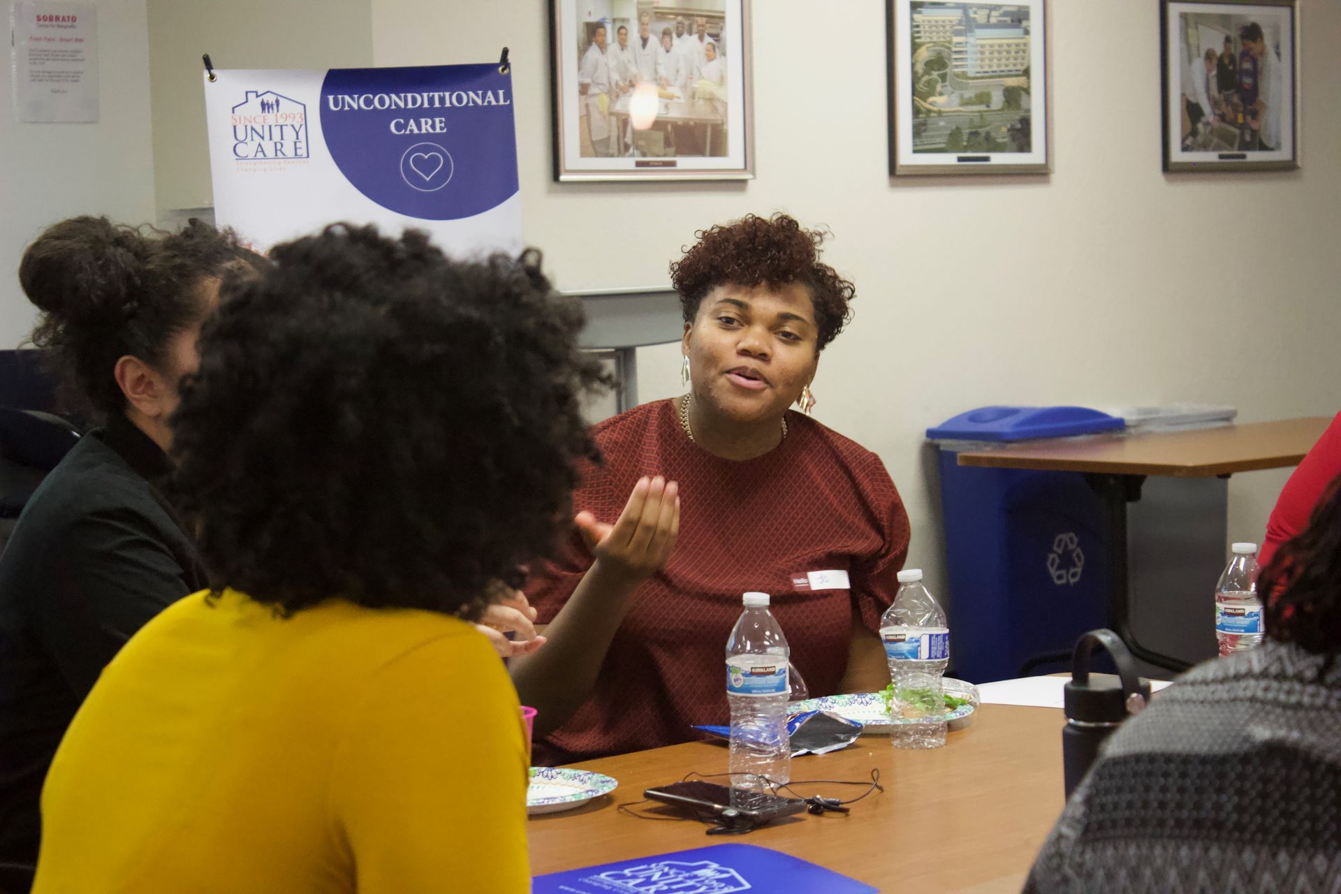 People in a meeting room talking around a table with water bottles and papers.