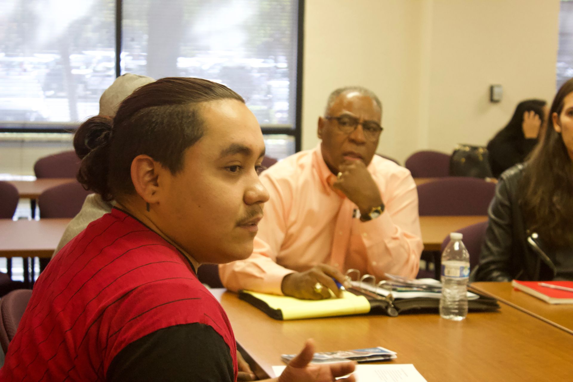 Three people seated at a conference table in a meeting room, with notebooks and a water bottle.