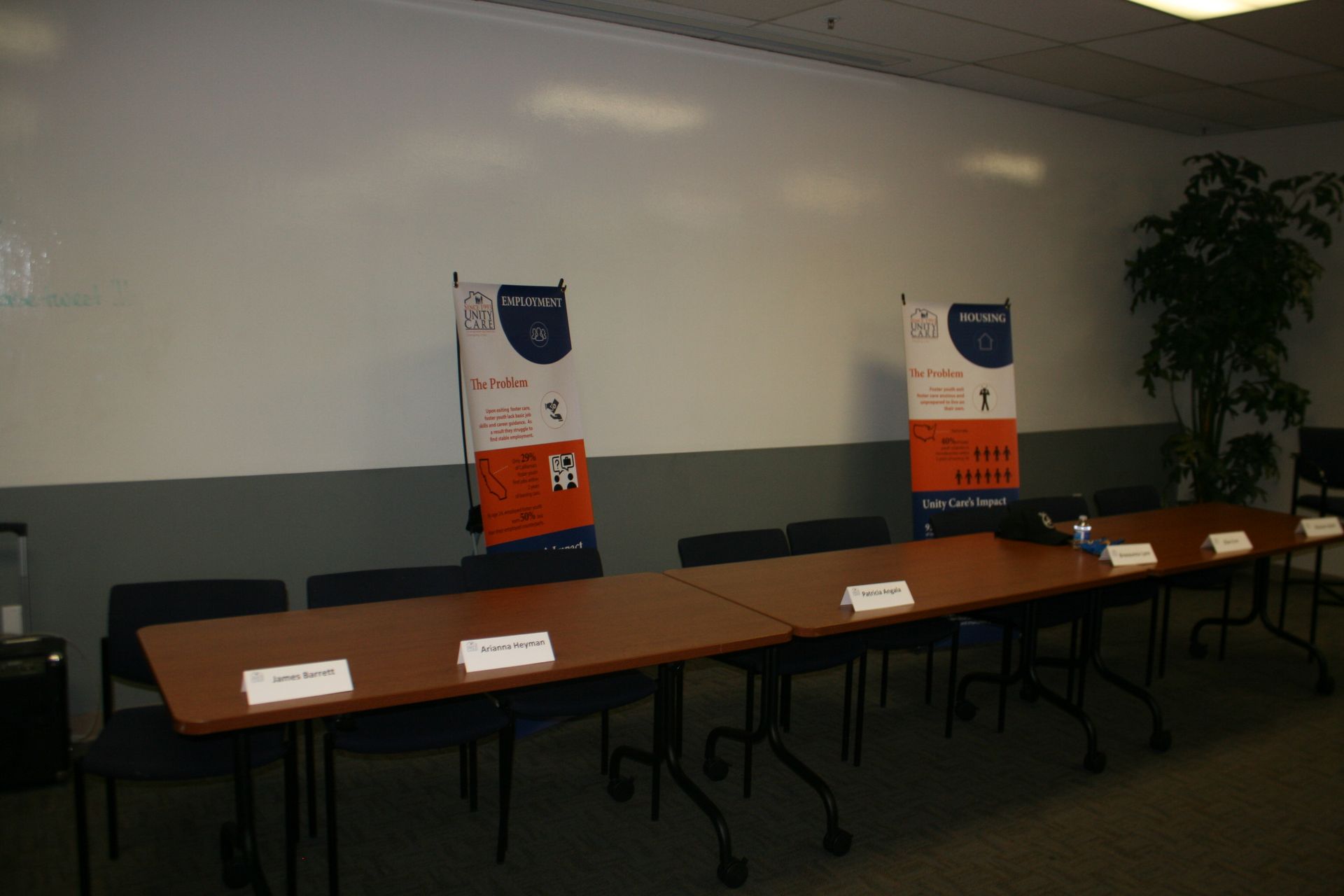 Conference room with long table, name placards, and two standing banners against a blank wall.