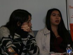 Two women seated indoors, one listening with her hand on her chin while the other speaks.