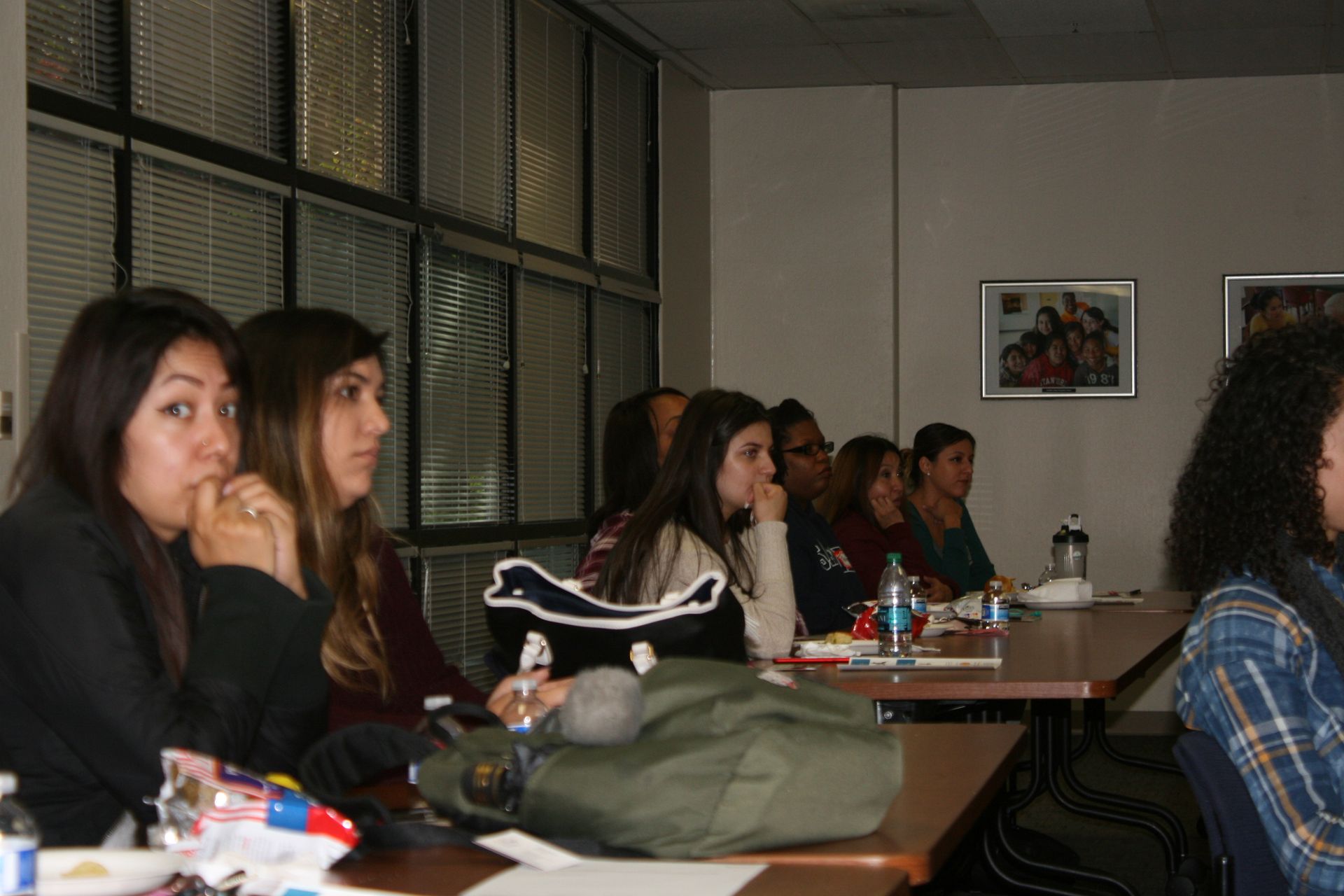 People seated at tables in a classroom, listening during a meeting or lecture.