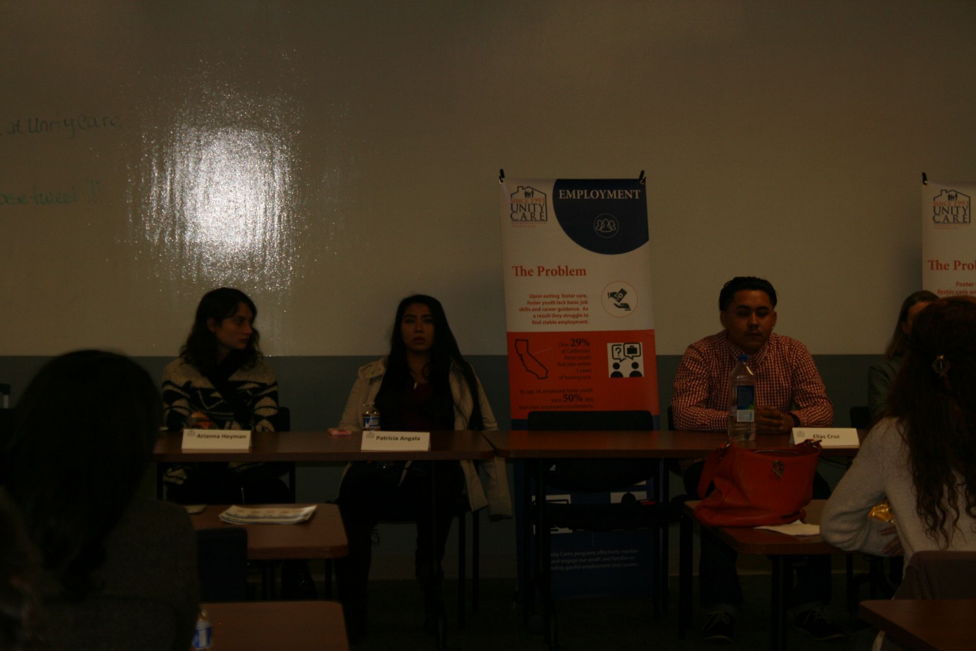 Panel discussion with three speakers seated at a table beside a poster in a dim room