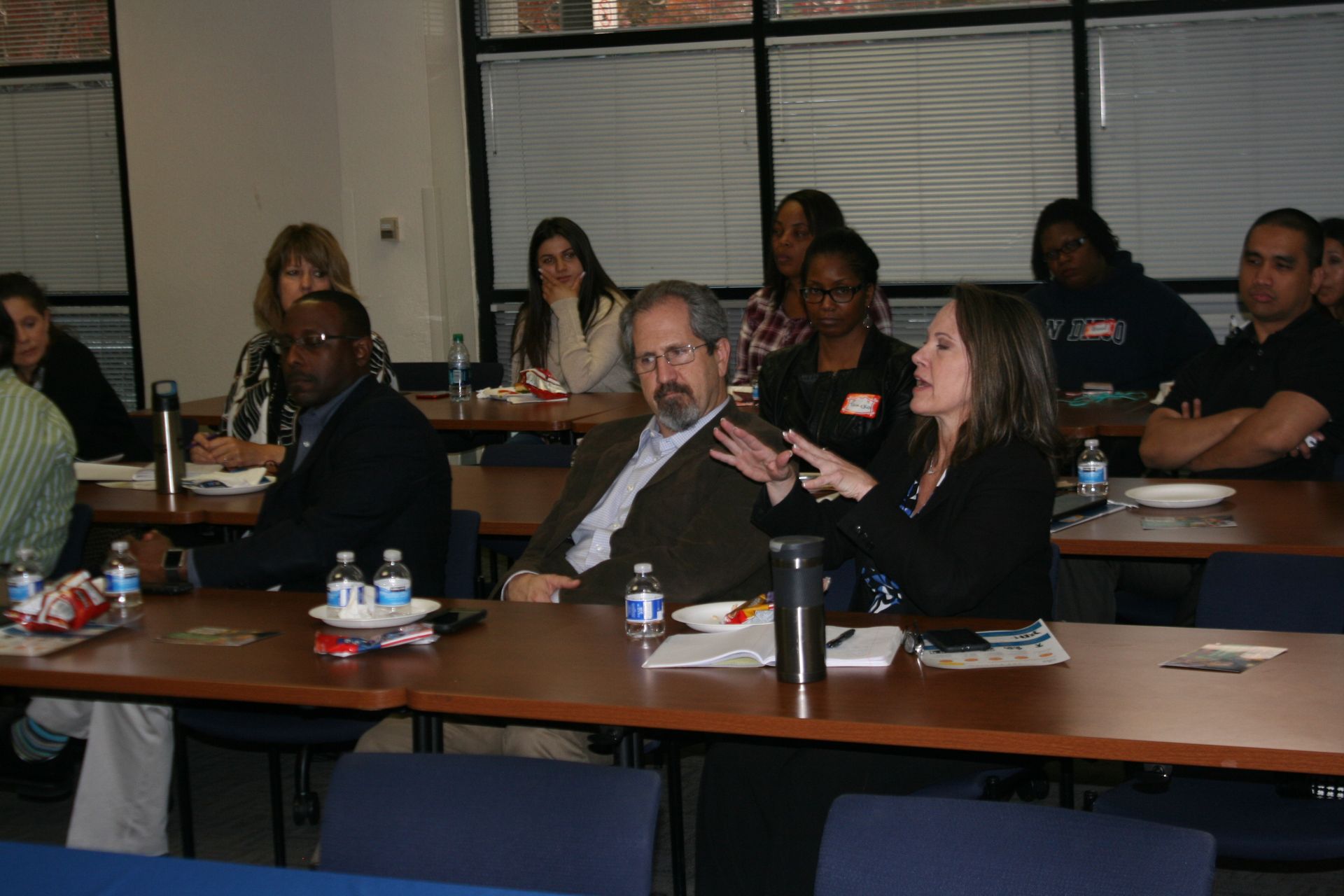Audience seated at a conference table in a meeting room, listening and taking notes.