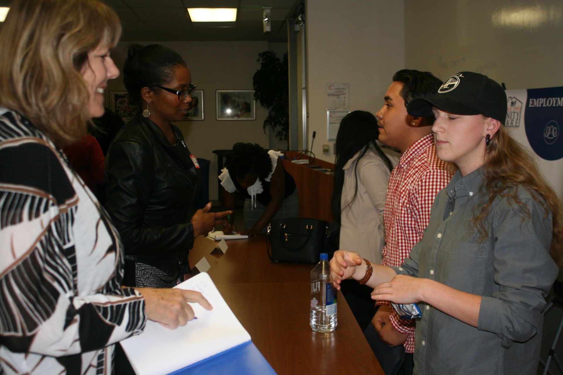 People standing at a table during an indoor event, talking and exchanging items