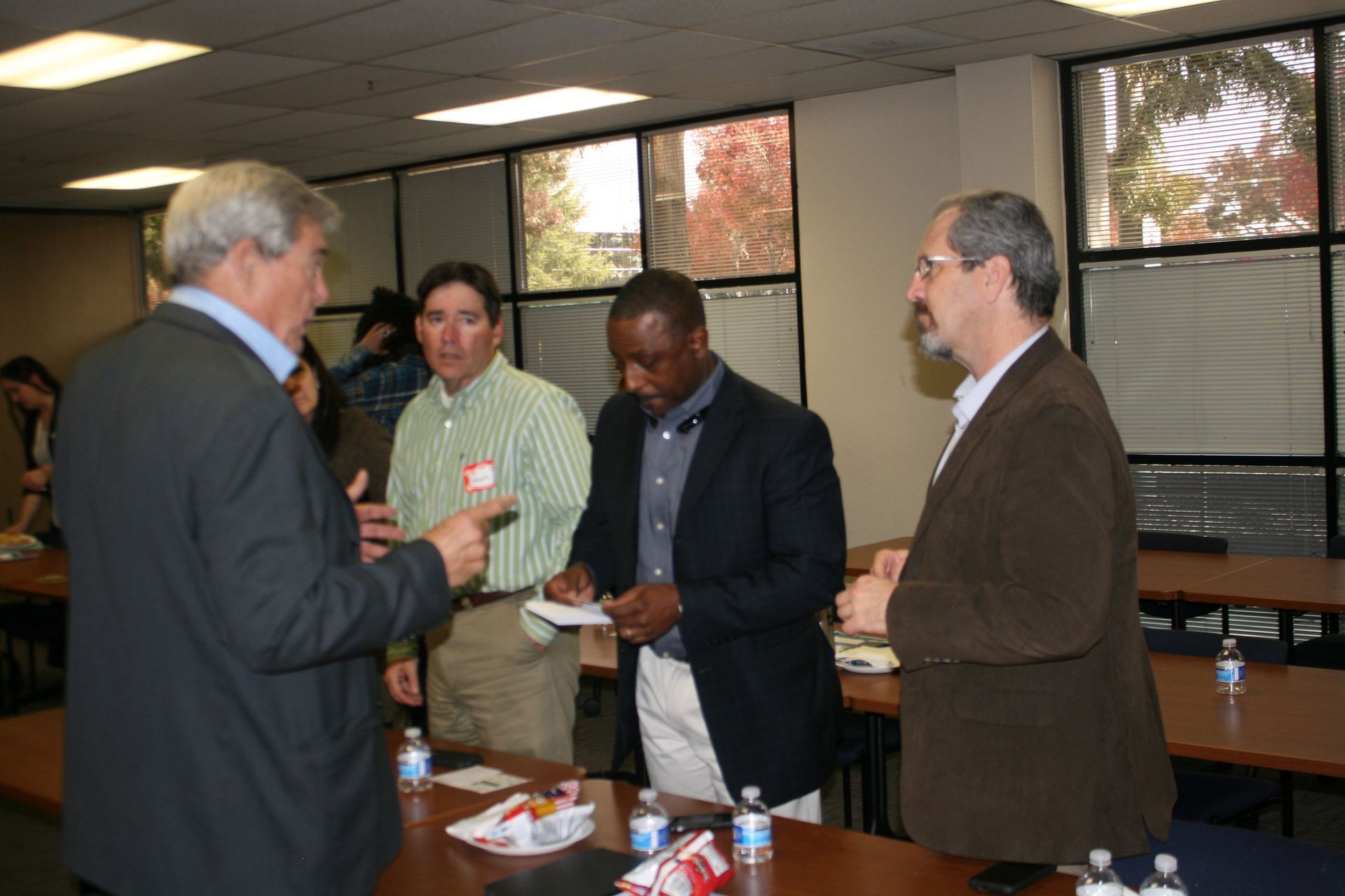 Four men in business attire converse at a table in a conference room.