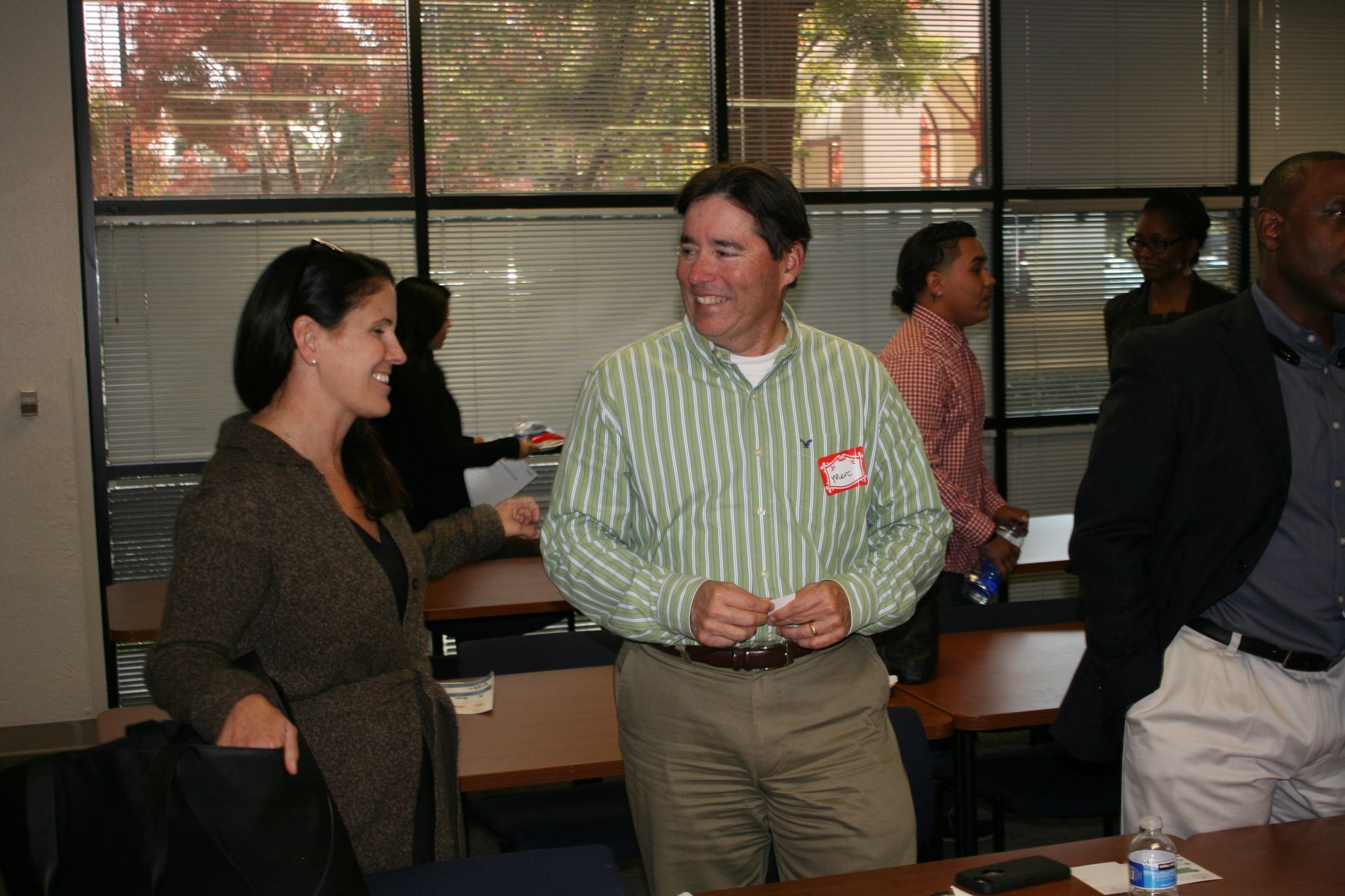 Two people chatting in an office, one holding a drink, with large windows in the background.