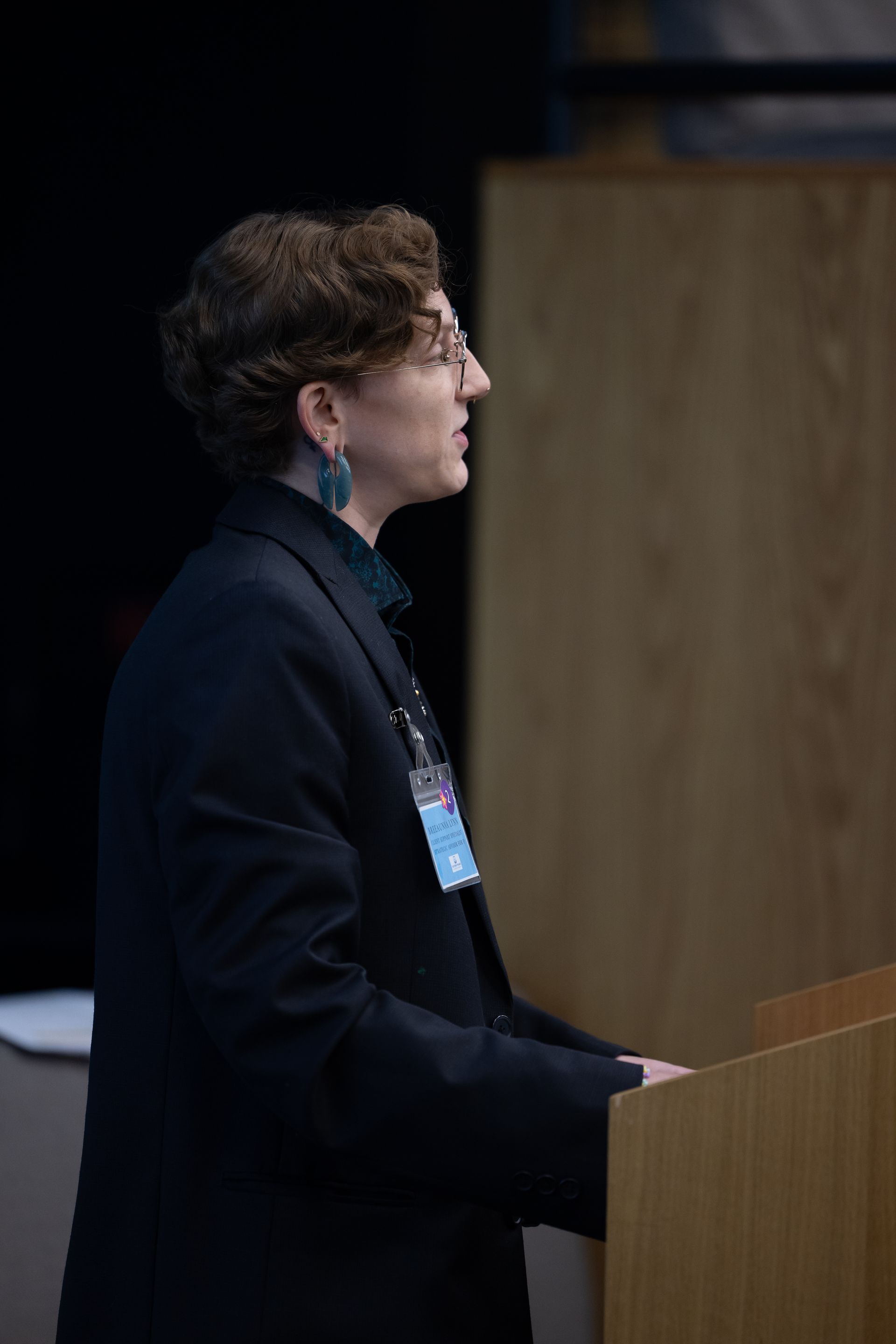 Person speaking at a podium in a dark suit during a presentation.