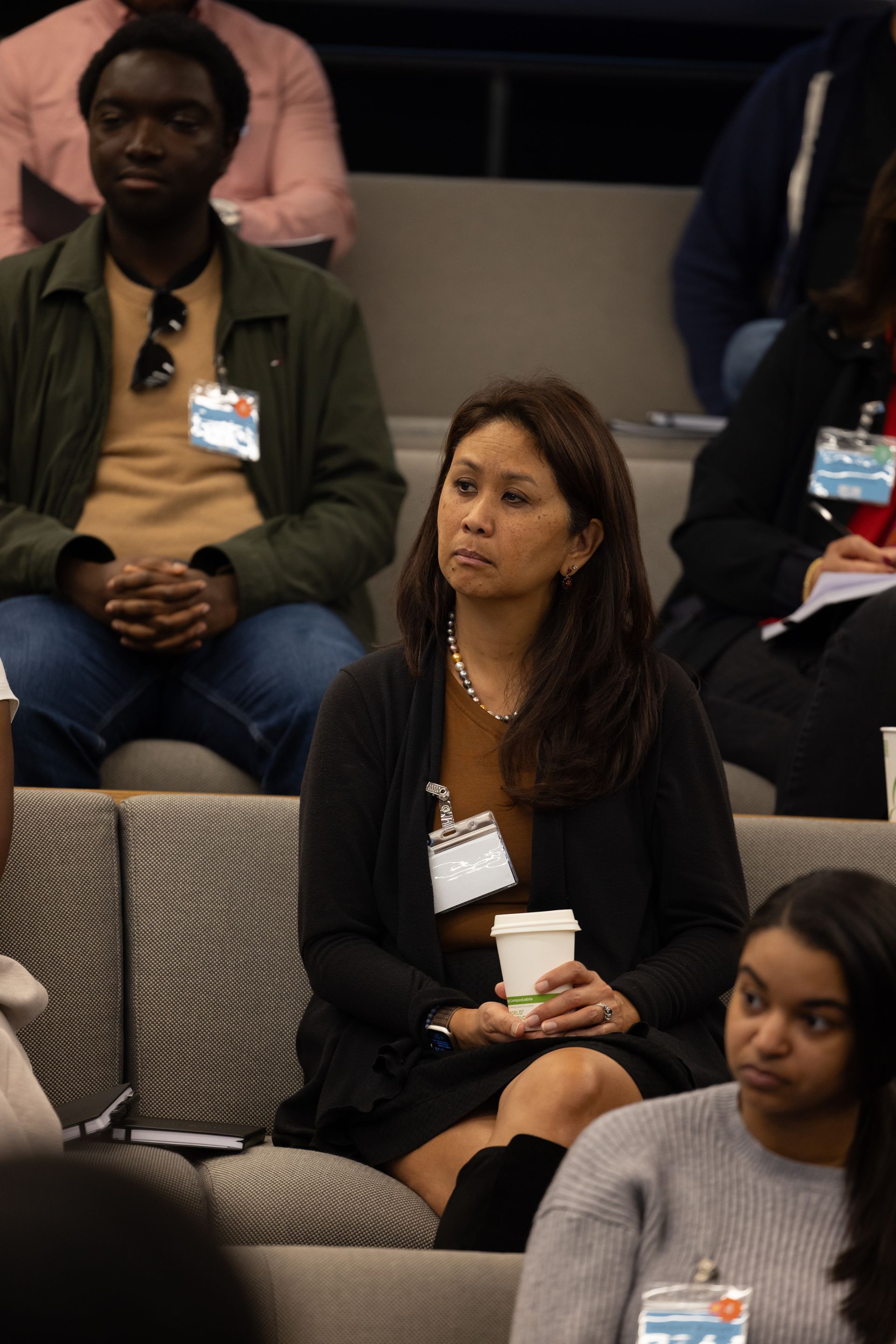 Audience seated in a conference room, listening attentively with name tags on.